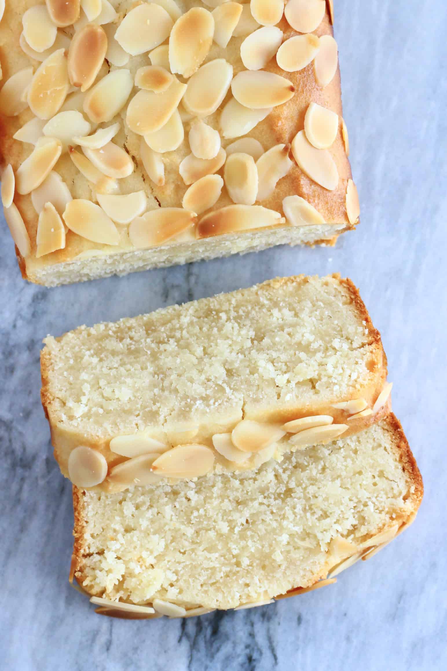 A gluten-free vegan almond loaf cake with two slices cut from it on a marble background
