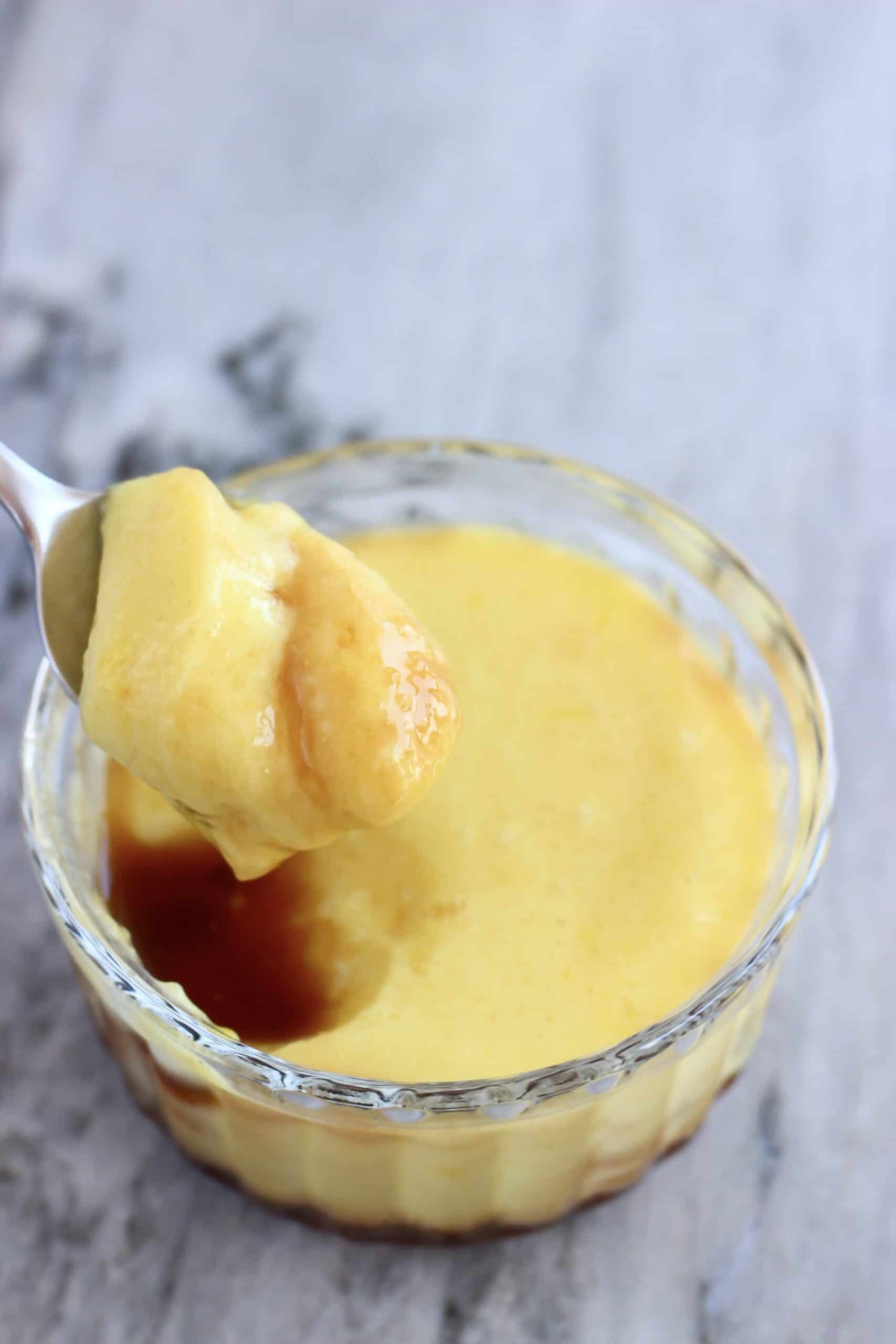 A vegan crème caramel in a glass pot with a spoon lifting out a mouthful