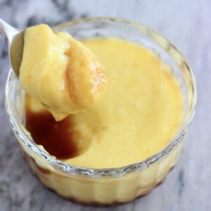 A vegan crème caramel in a glass pot with a spoon lifting out a mouthful