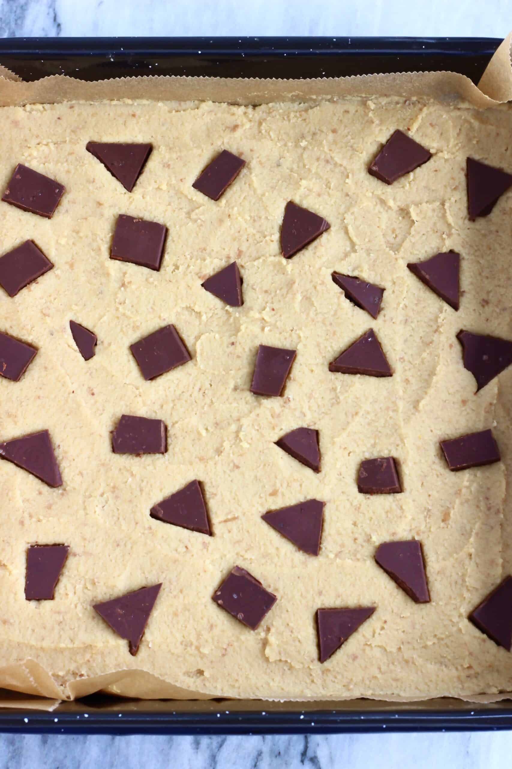 Raw chickpea blondies batter in a square baking tin lined with baking paper topped with chocolate chunks