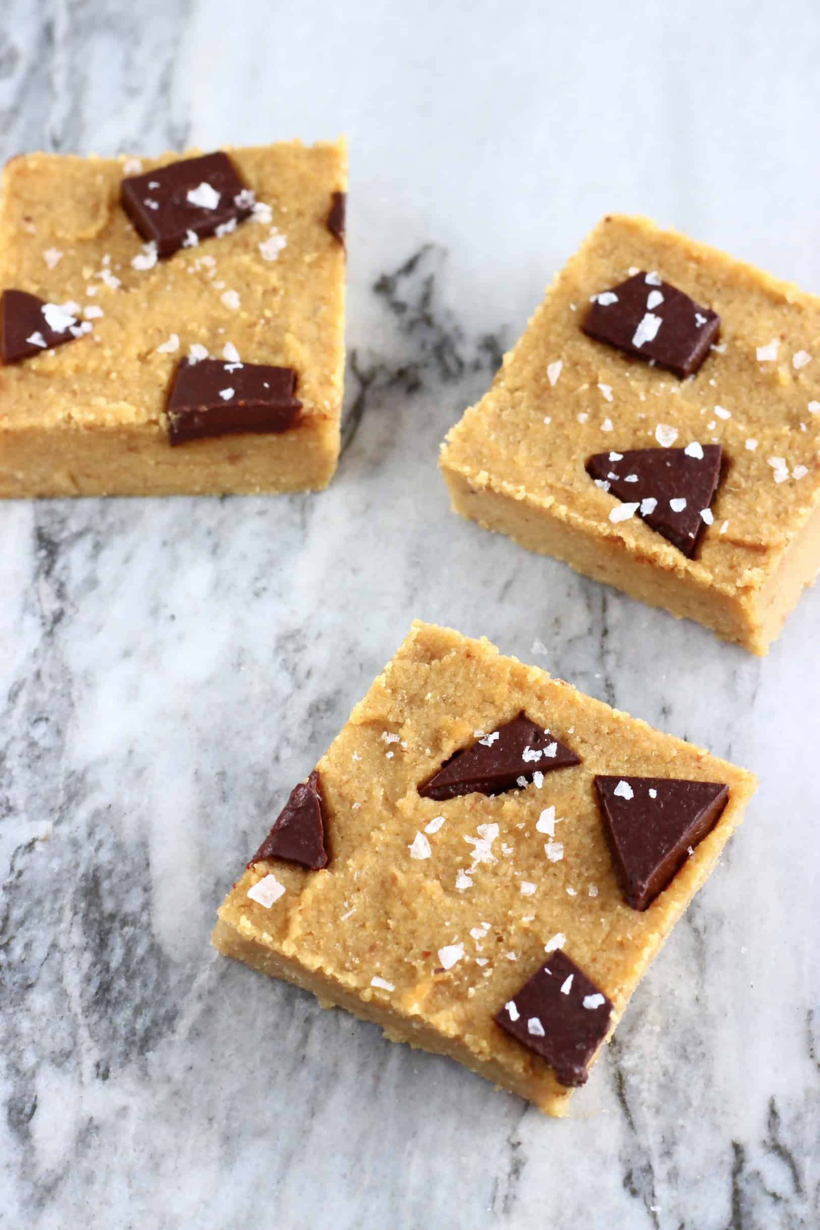 Three chickpea blondies with chocolate chunks topped with sea salt on a marble background