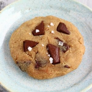 A chickpea cookie with chocolate chips on a plate sprinkled with sea salt flakes
