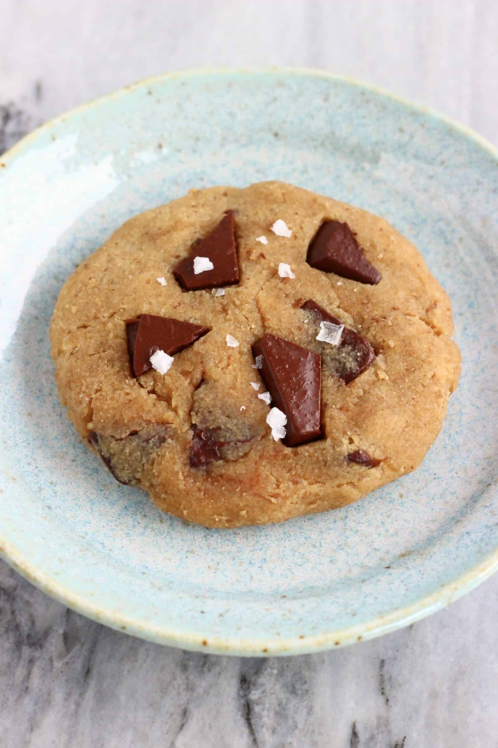A chickpea cookie with chocolate chips on a plate sprinkled with sea salt flakes
