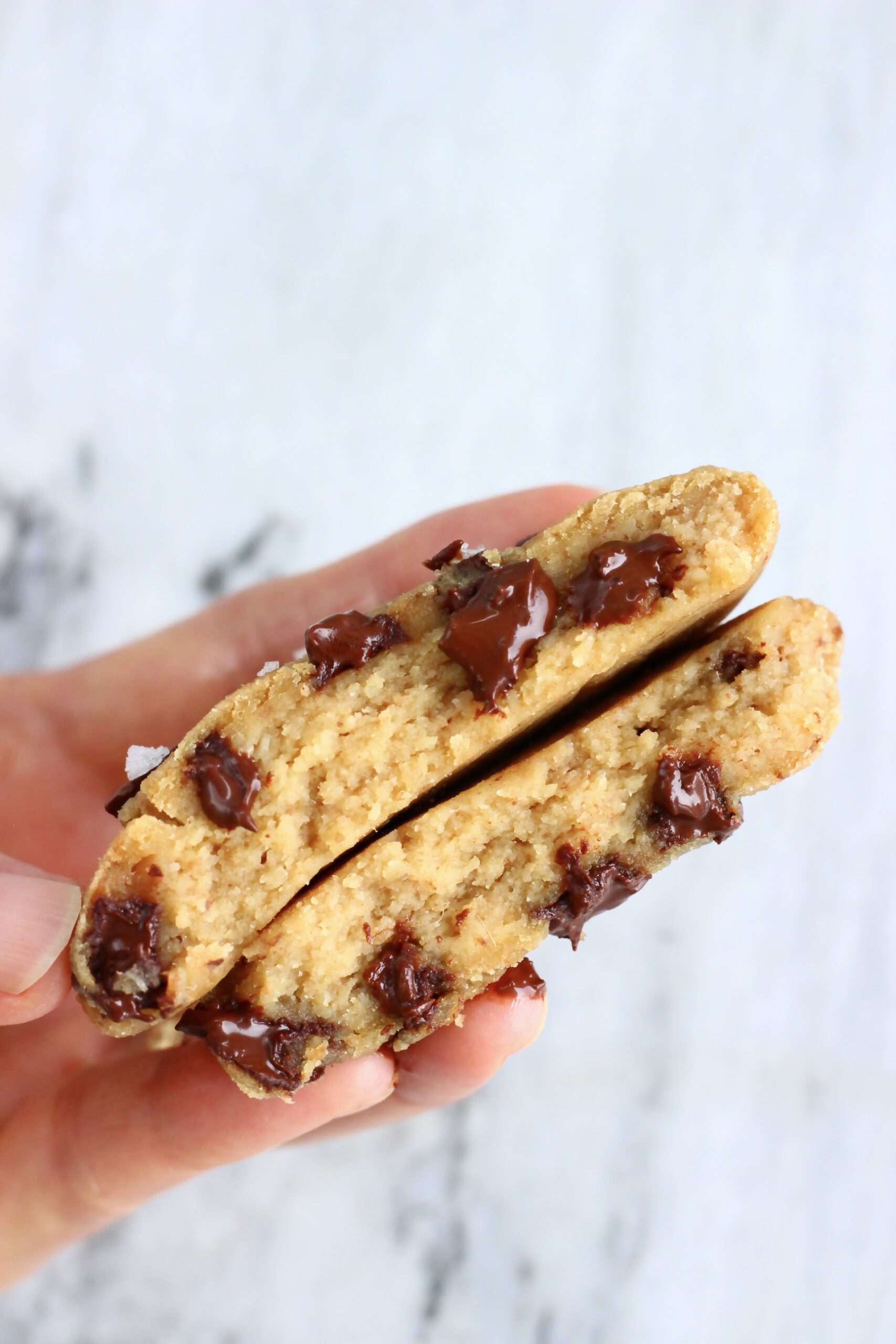 Two halves of a chickpea cookie with chocolate chips being held up by a hand