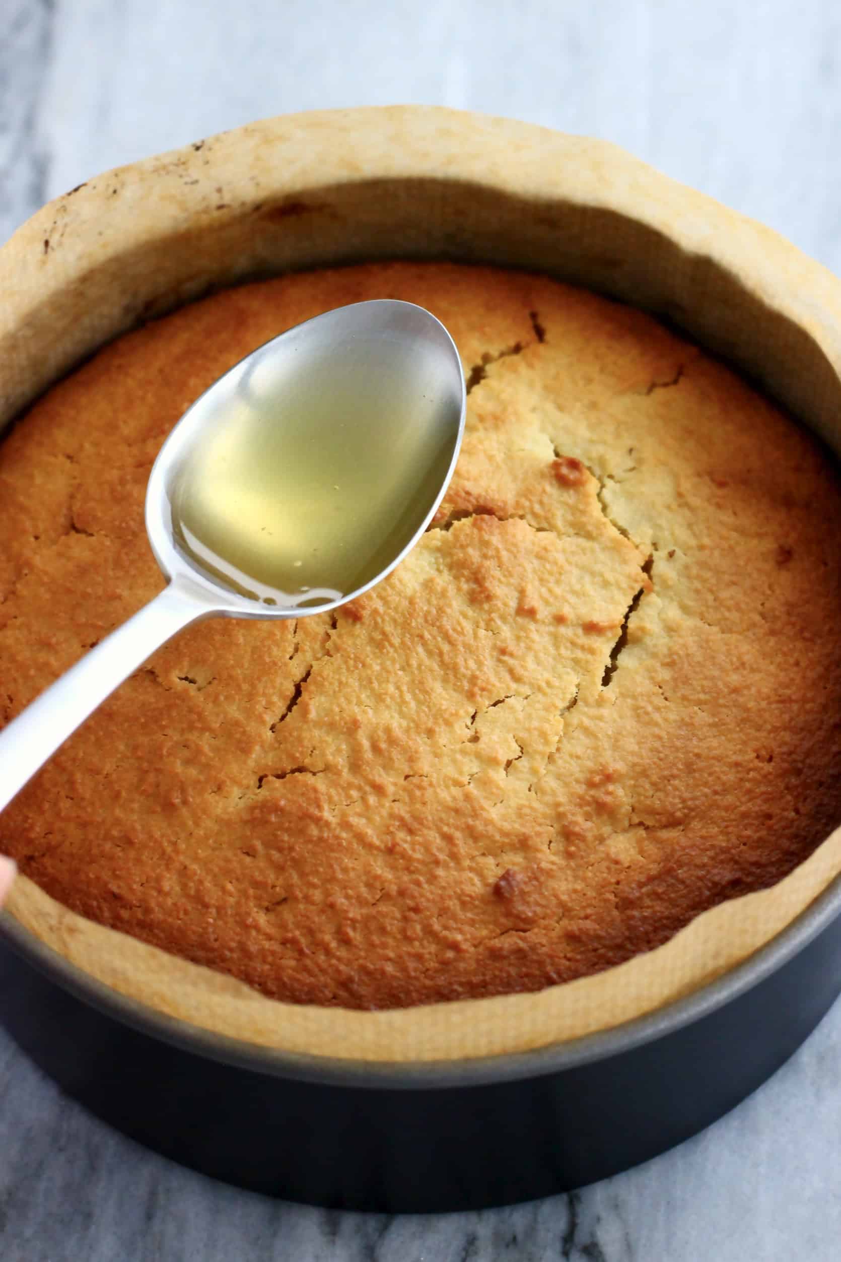 A baked gluten-free vegan lemon olive oil cake with lemon syrup being drizzled over it with a spoon