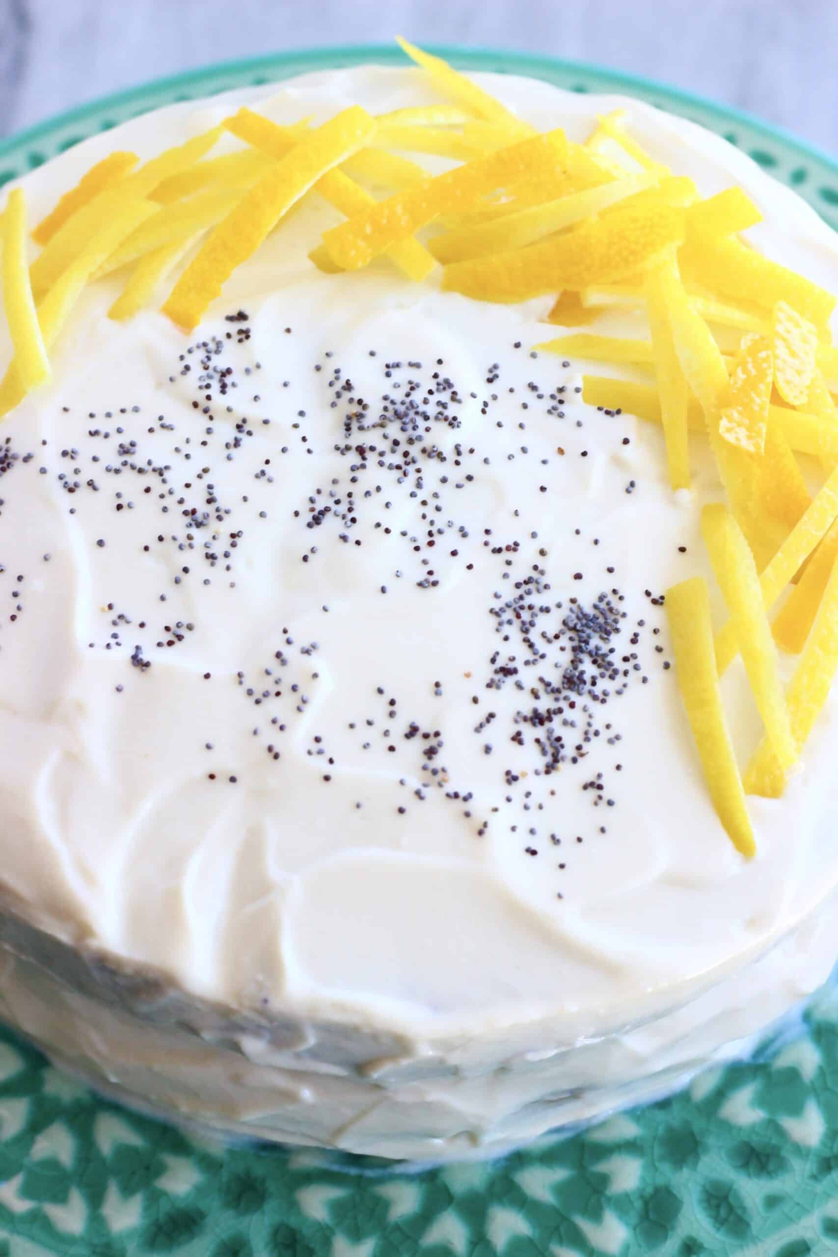 A vegan lemon poppy seed layer cake covered in frosting and decorated with poppy seeds and lemon peel