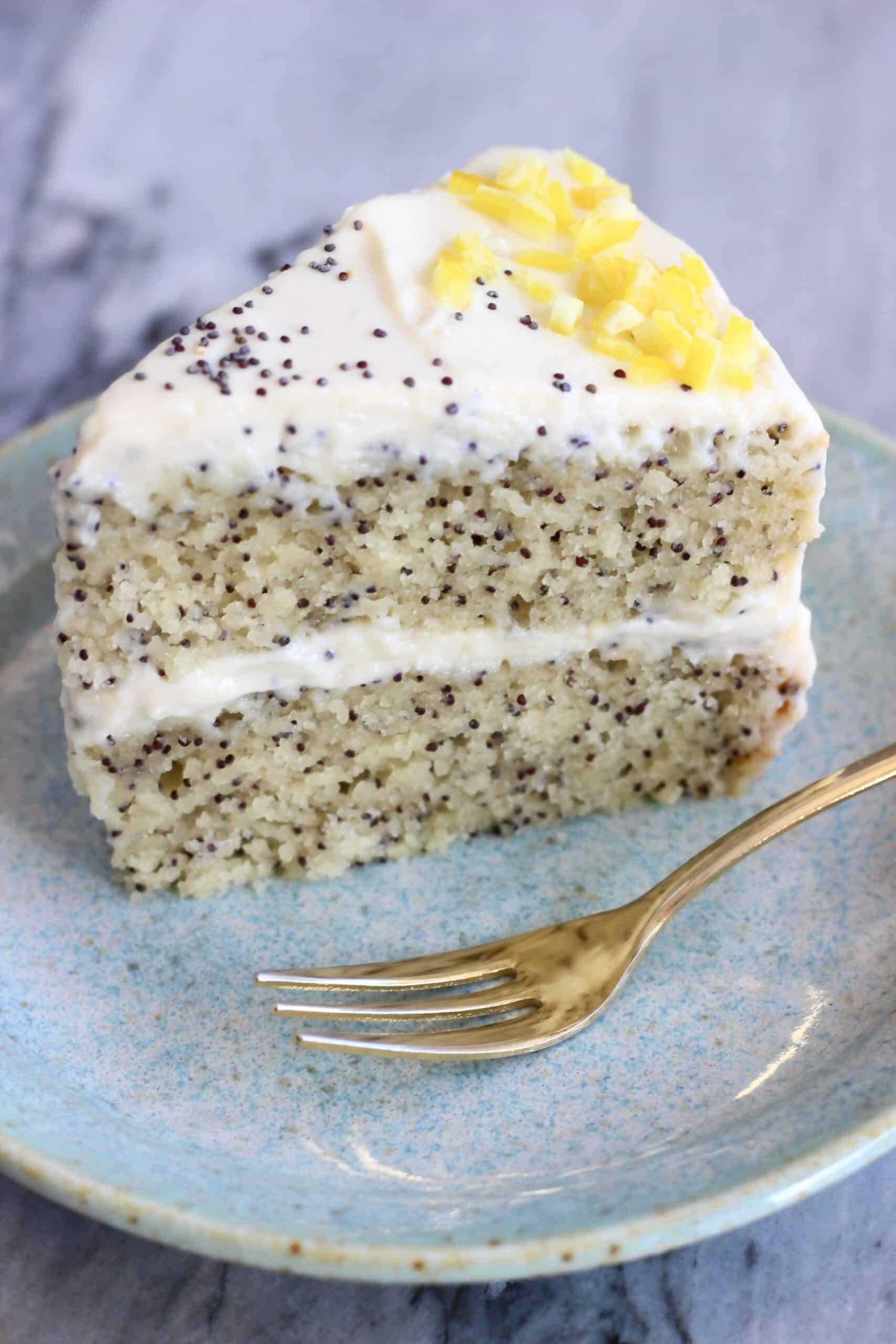 A slice of vegan lemon poppy seed layer cake on a plate with a fork