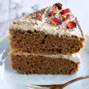 A slice of vegan hojicha latte cake topped with rose petals on a plate with a fork
