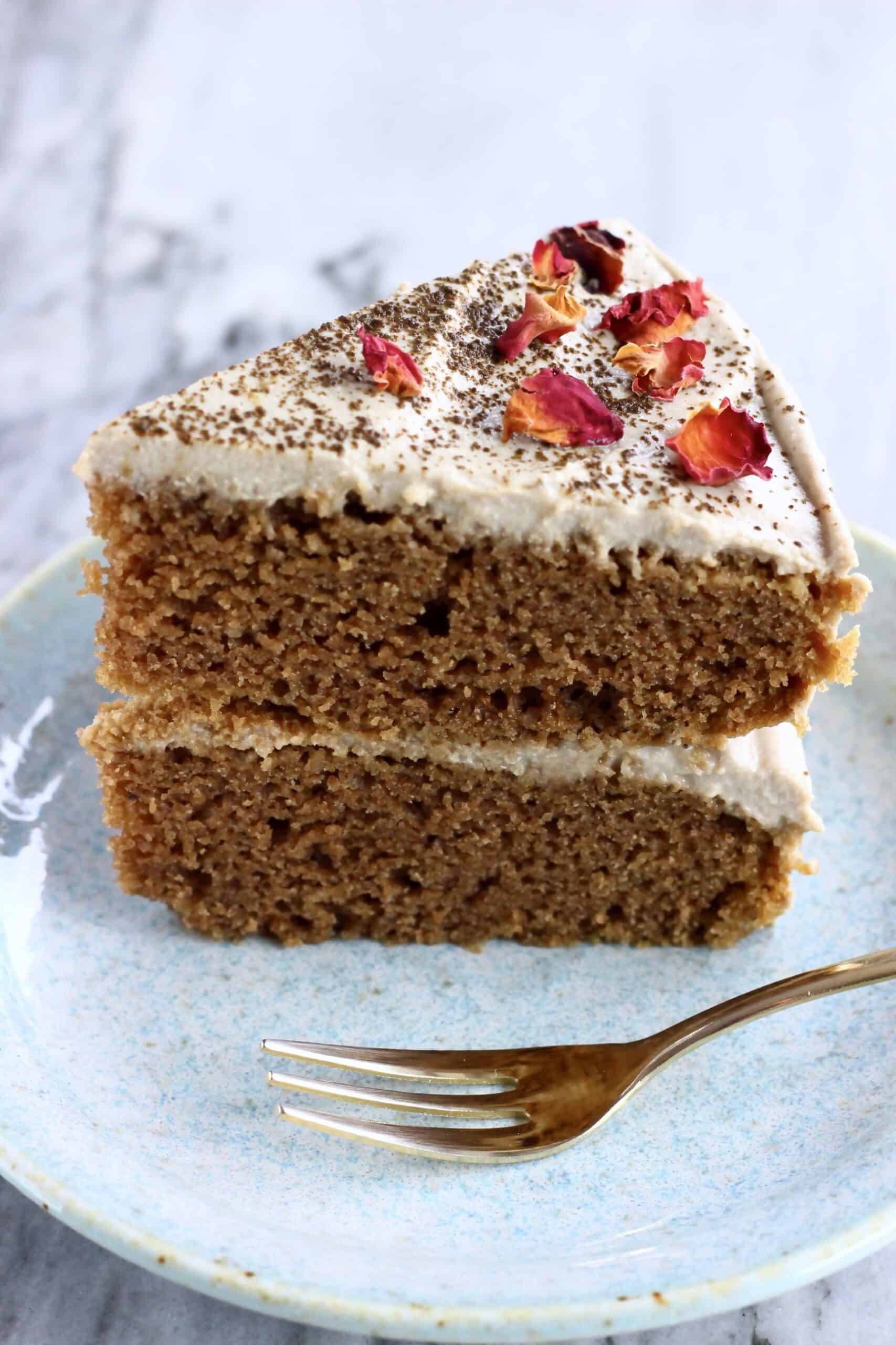 A slice of vegan hojicha latte cake topped with rose petals on a plate with a fork