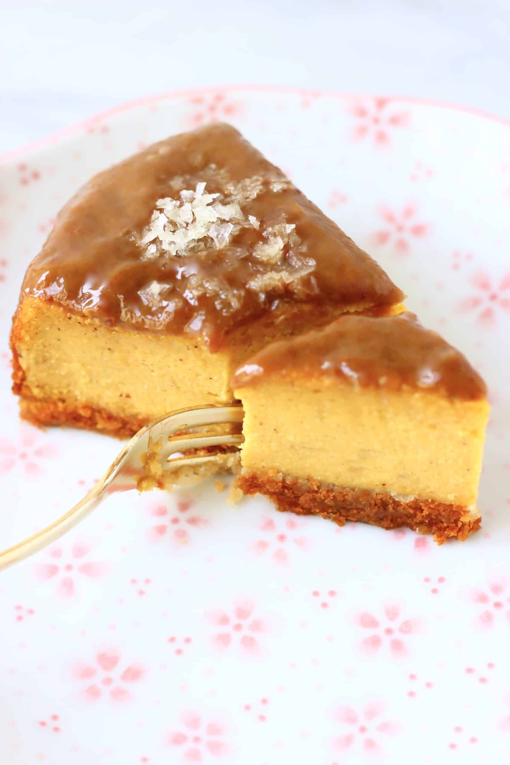 A slice of vegan baked pumpkin cheesecake topped with caramel sauce and salt with a fork taking a bite out of it