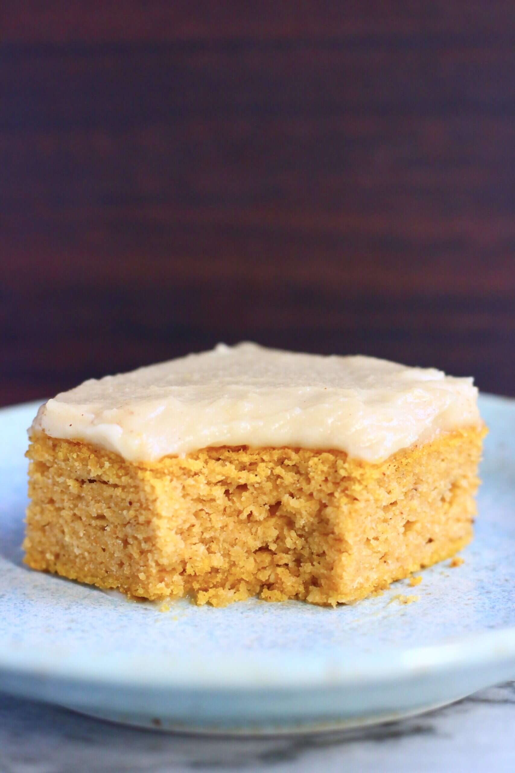 A square of gluten-free vegan pumpkin bars topped with frosting with a mouthful taken out of it on a blue plate