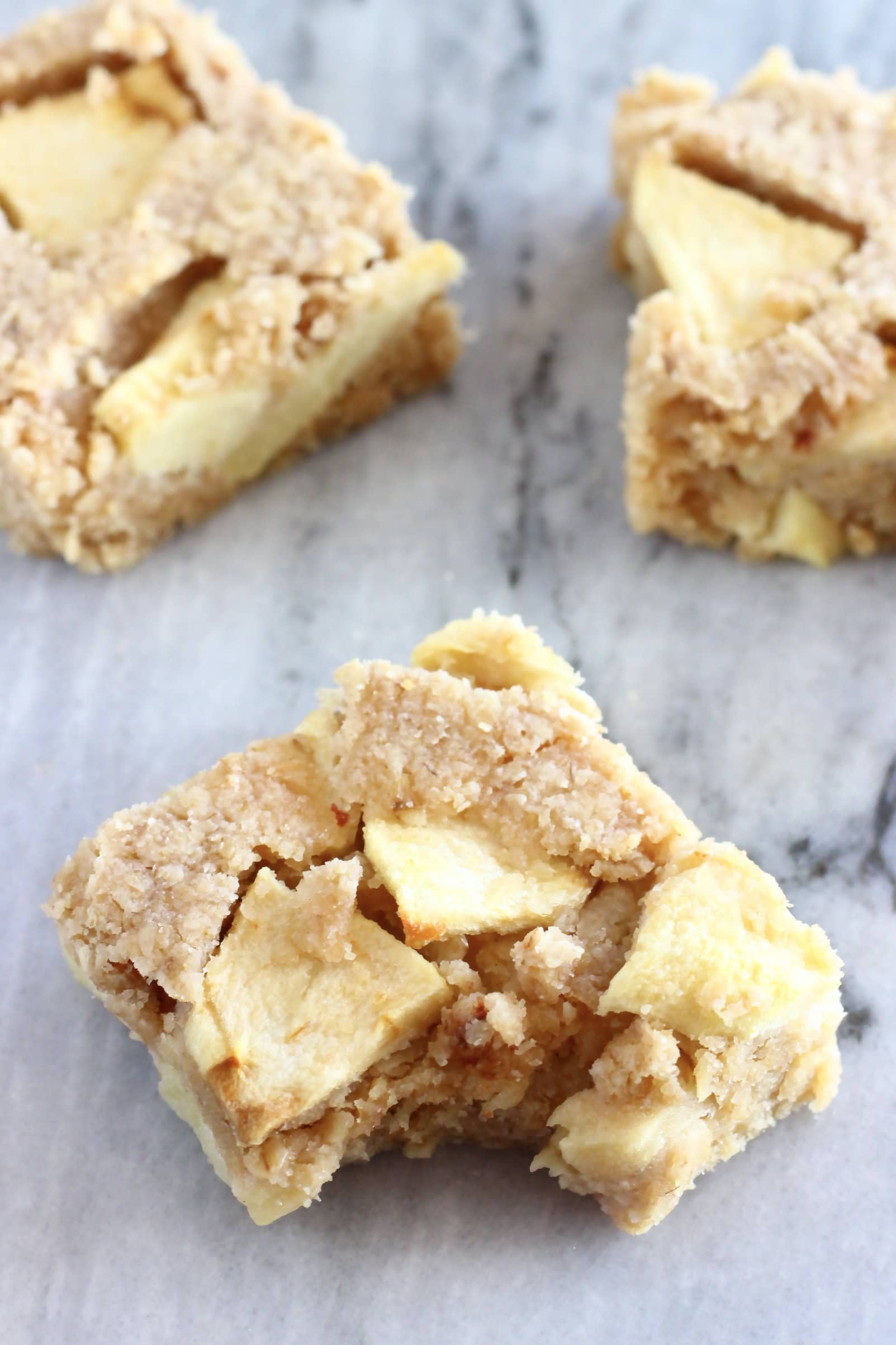 Three vegan apple oatmeal bars with a bite taken out of one on a marble background
