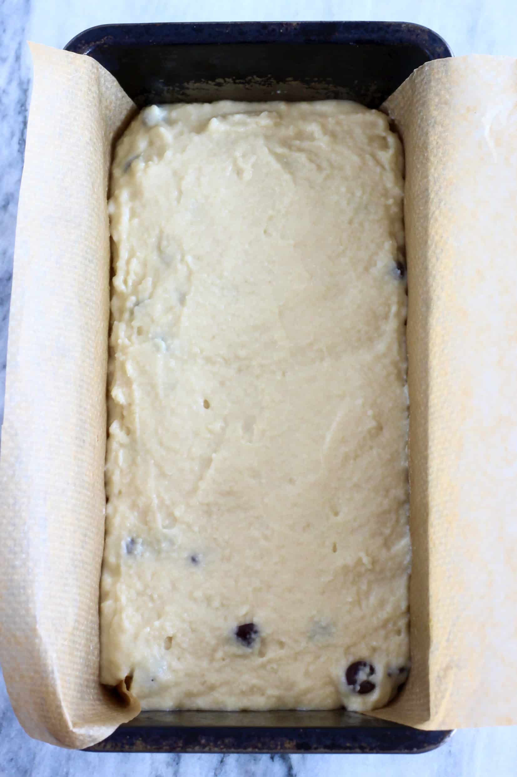 Raw gluten-free vegan chocolate chip bread batter in a loaf tin lined with baking paper