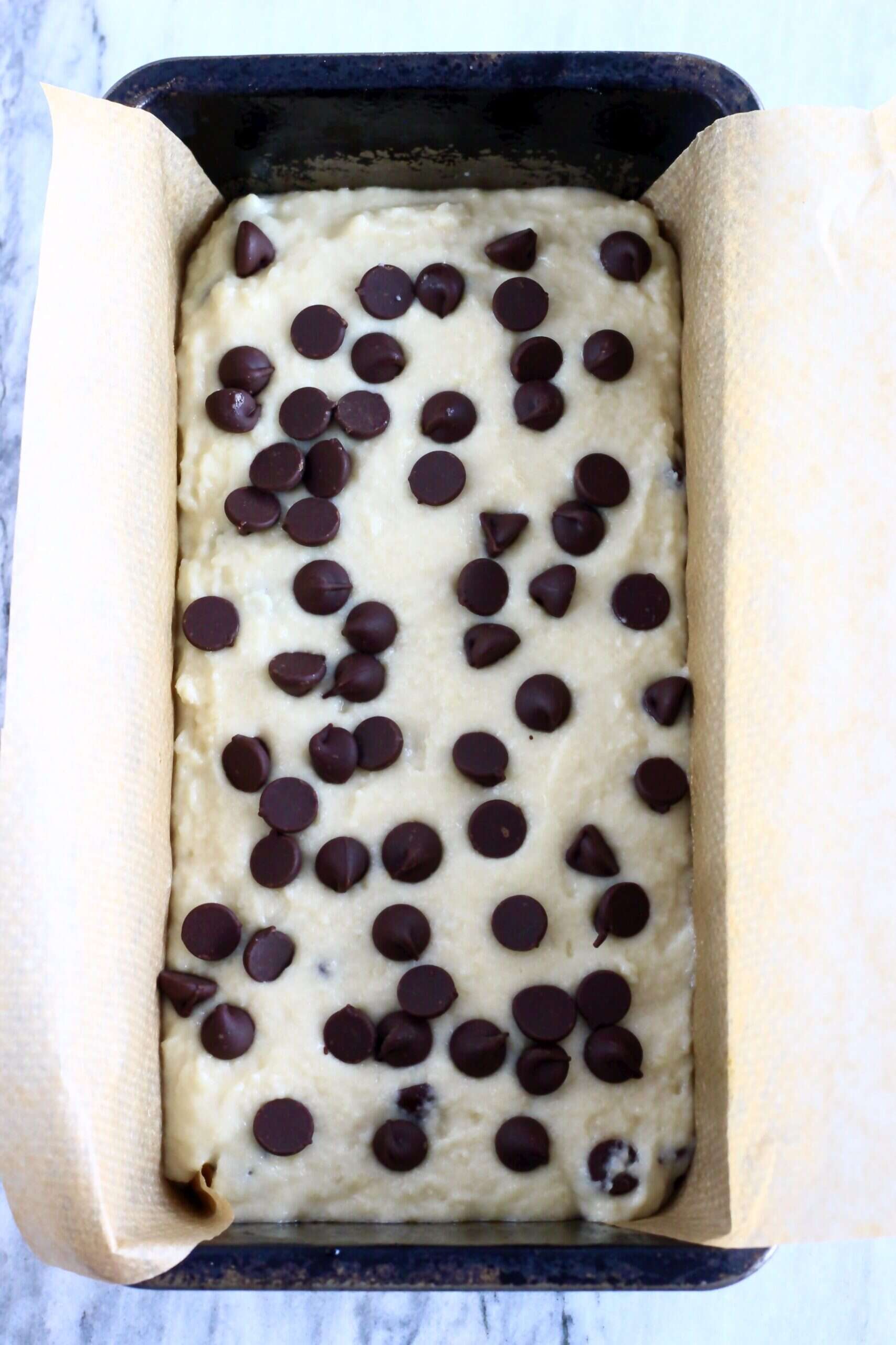 Raw gluten-free vegan chocolate chip bread batter scattered with chocolate chips in a loaf tin lined with baking paper
