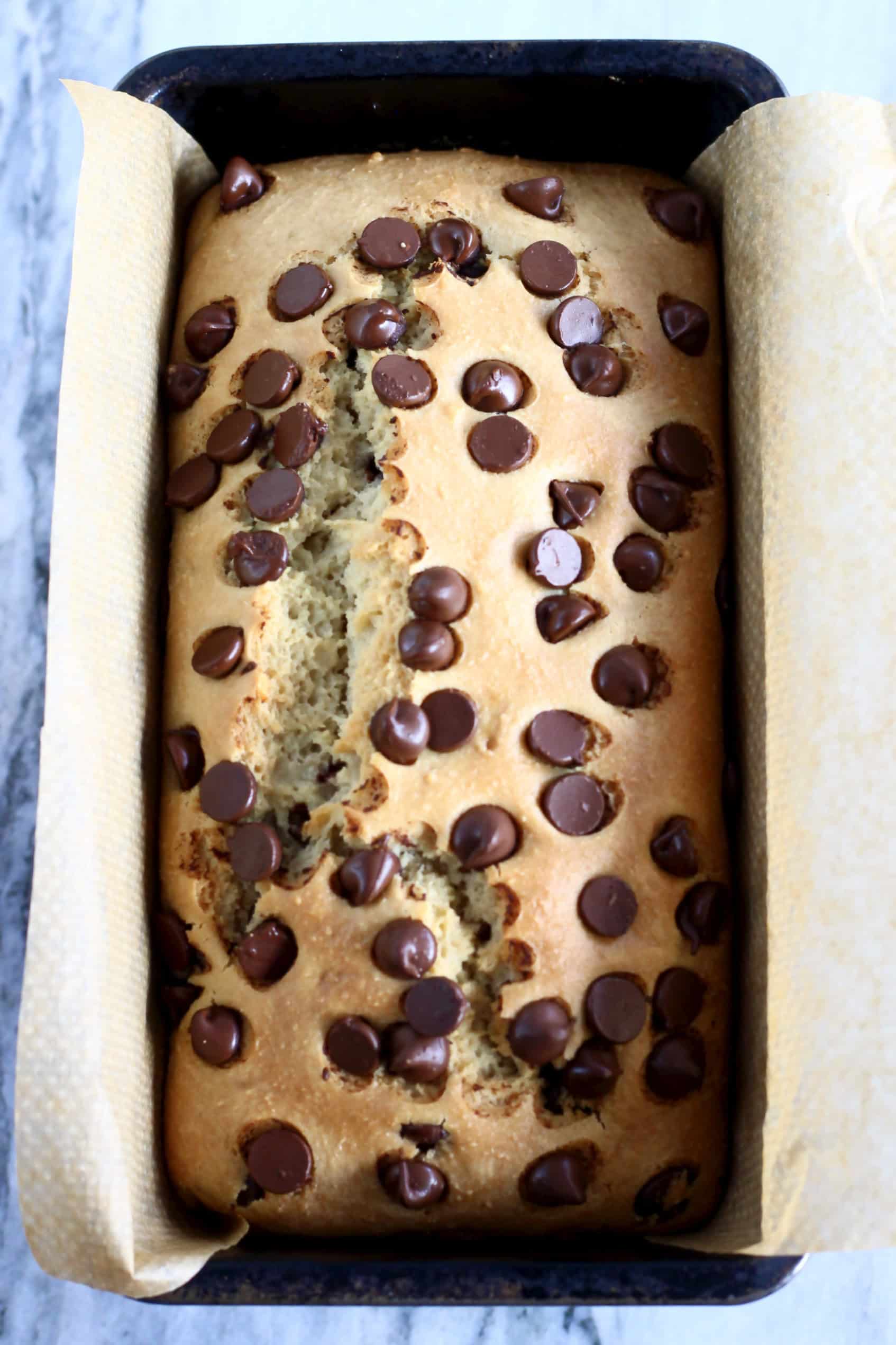 A baked loaf of gluten-free vegan chocolate chip bread in a loaf tin lined with baking paper