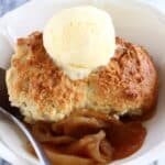 Gluten-free vegan apple cobbler in a bowl with a scoop of vanilla ice cream and a spoon