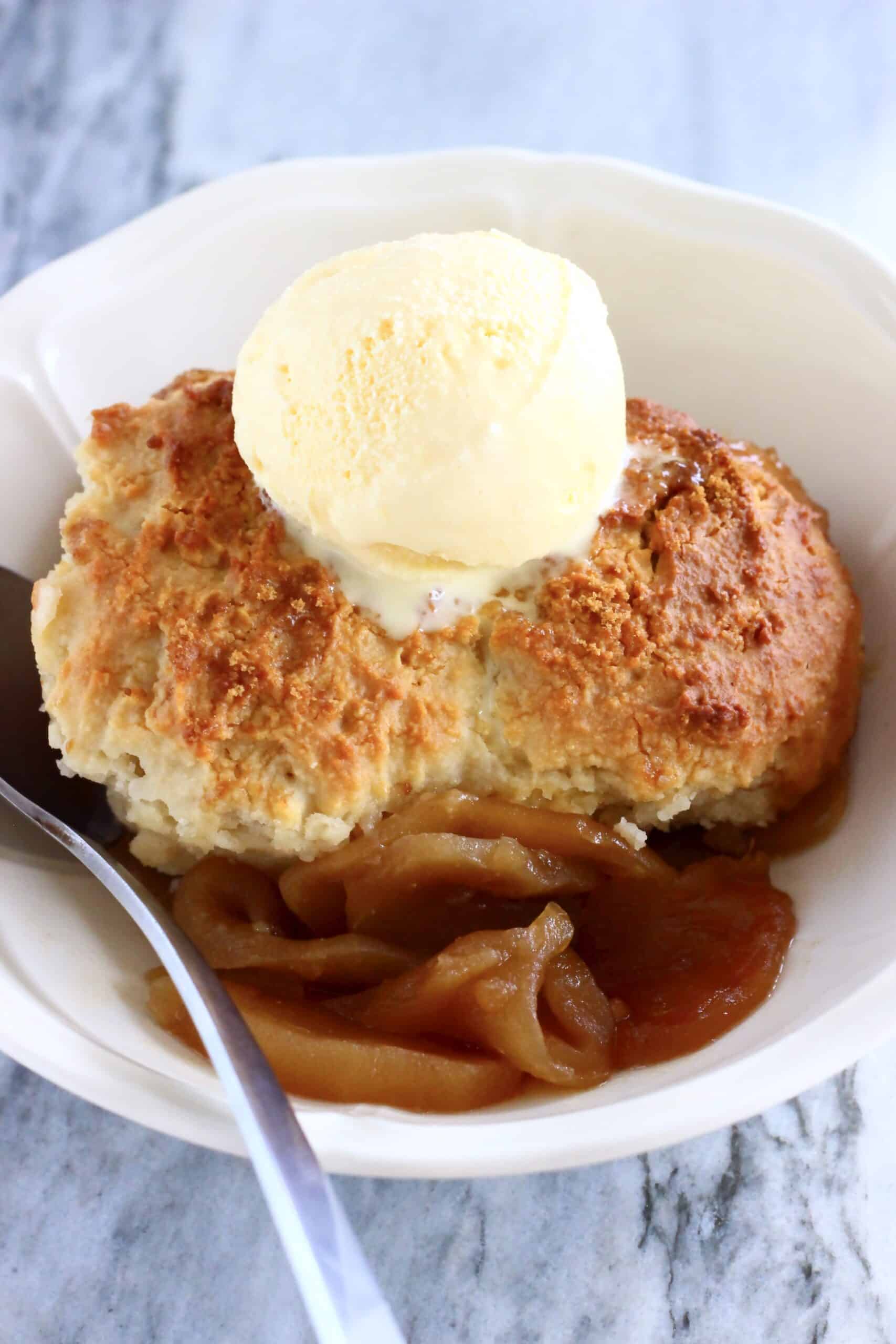 Gluten-free vegan apple cobbler in a bowl with a scoop of vanilla ice cream and a spoon