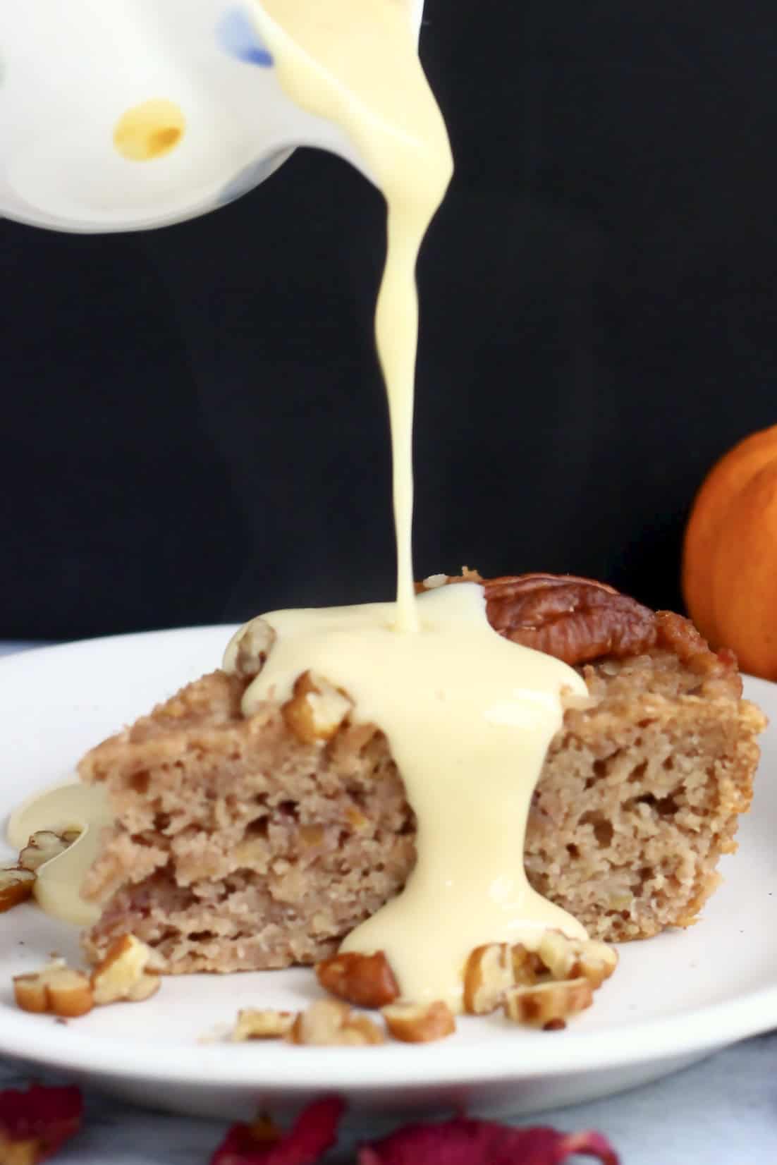 A slice of gluten-free vegan apple cake on a plate with custard being poured on top