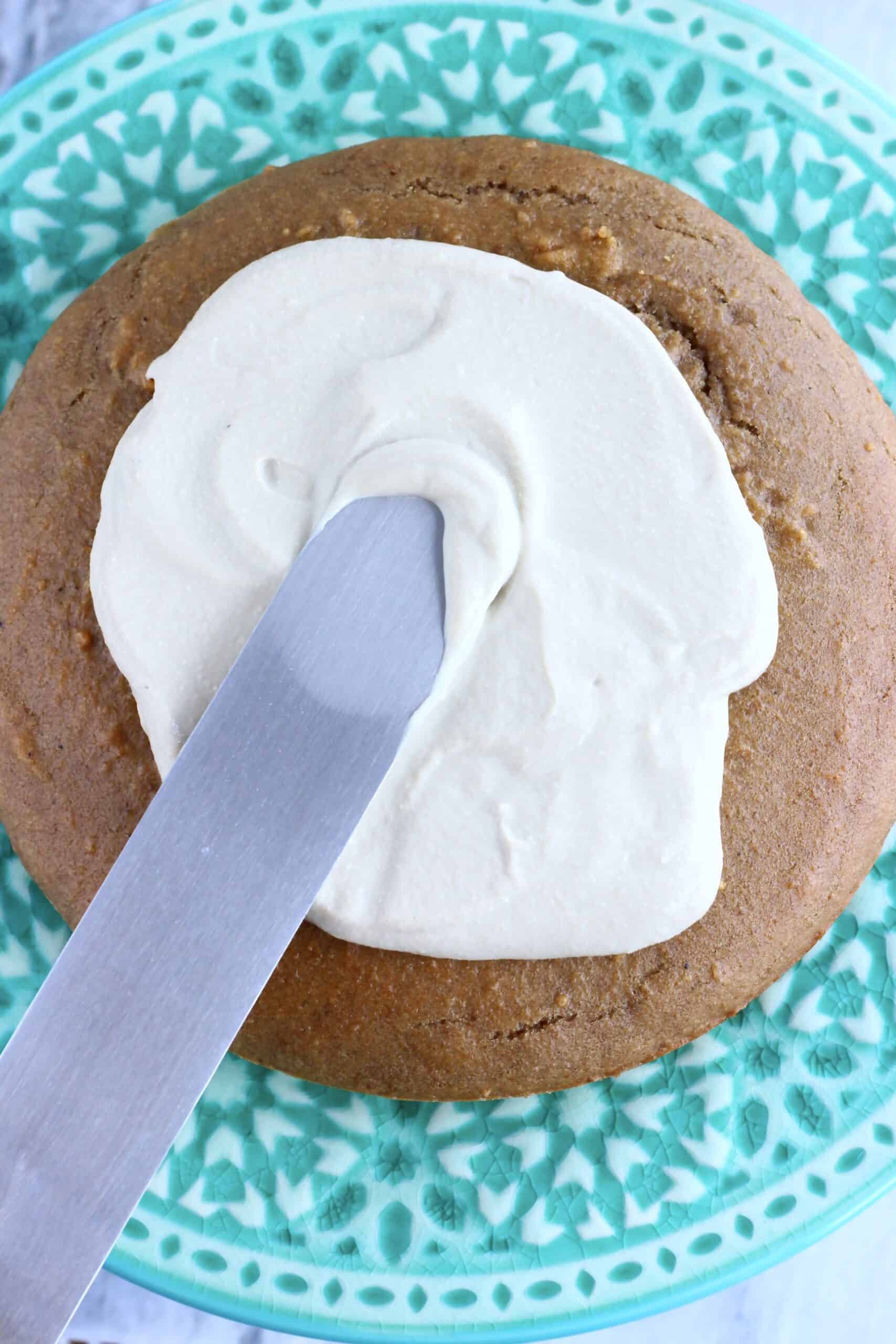 Vegan hojicha latte cake sponge on a cake stand with a palette knife spreading hojicha frosting over it