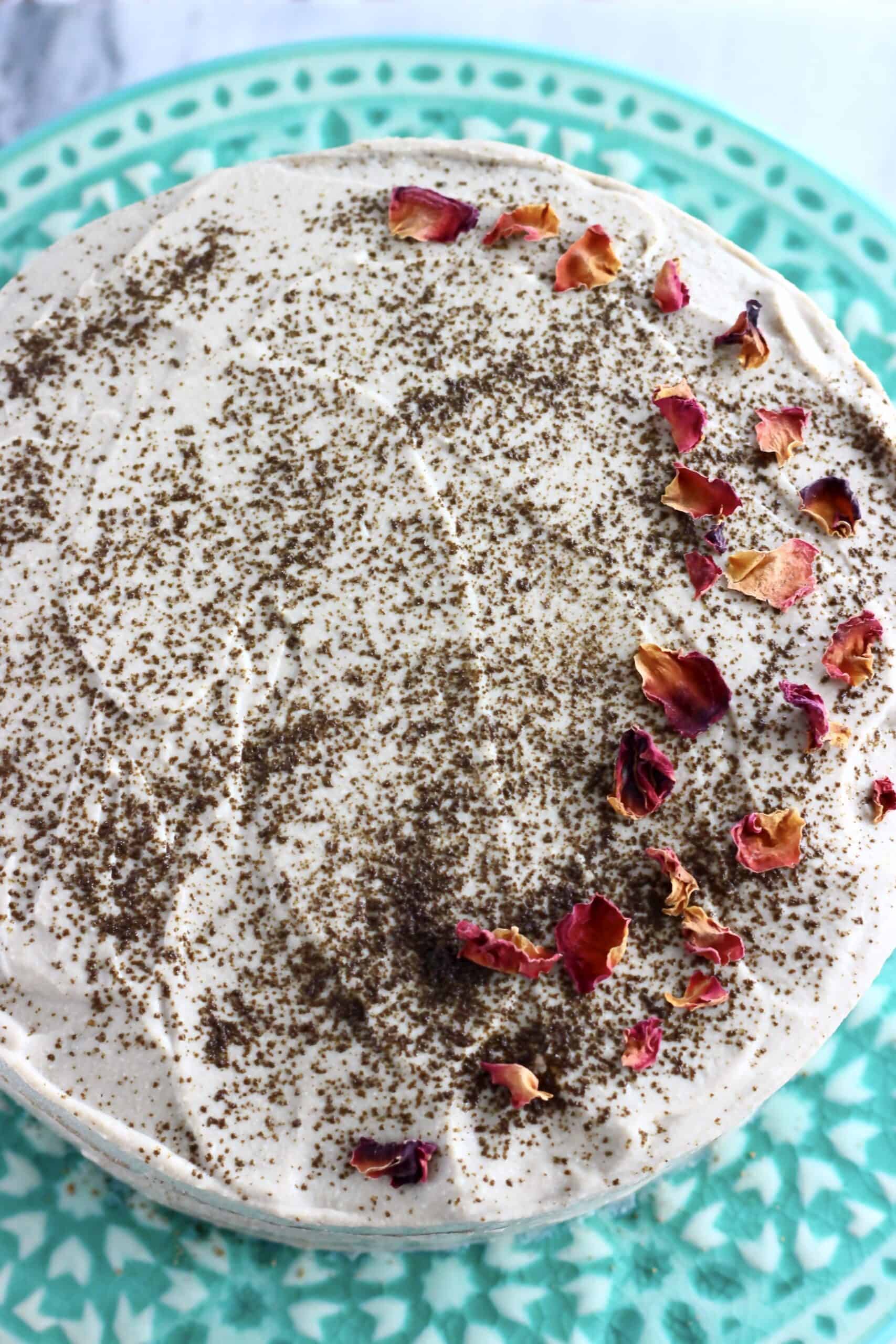 A vegan hojicha latte cake covered in frosting and decorated with hojicha powder and rose petals on a cake stand