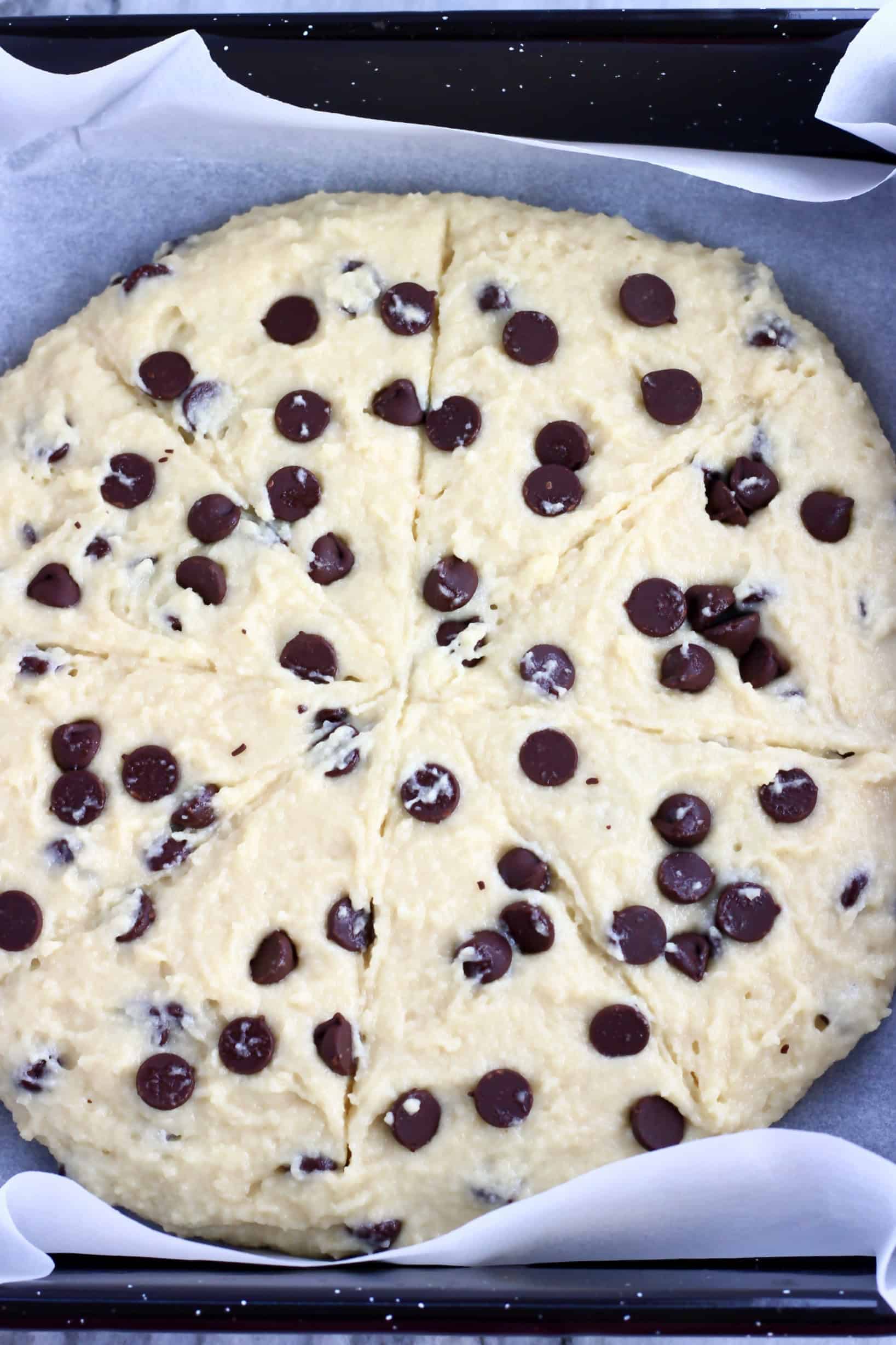 Raw gluten-free vegan chocolate chip scones dough in a circle carved into 8 pieces on a baking tray lined with baking paper