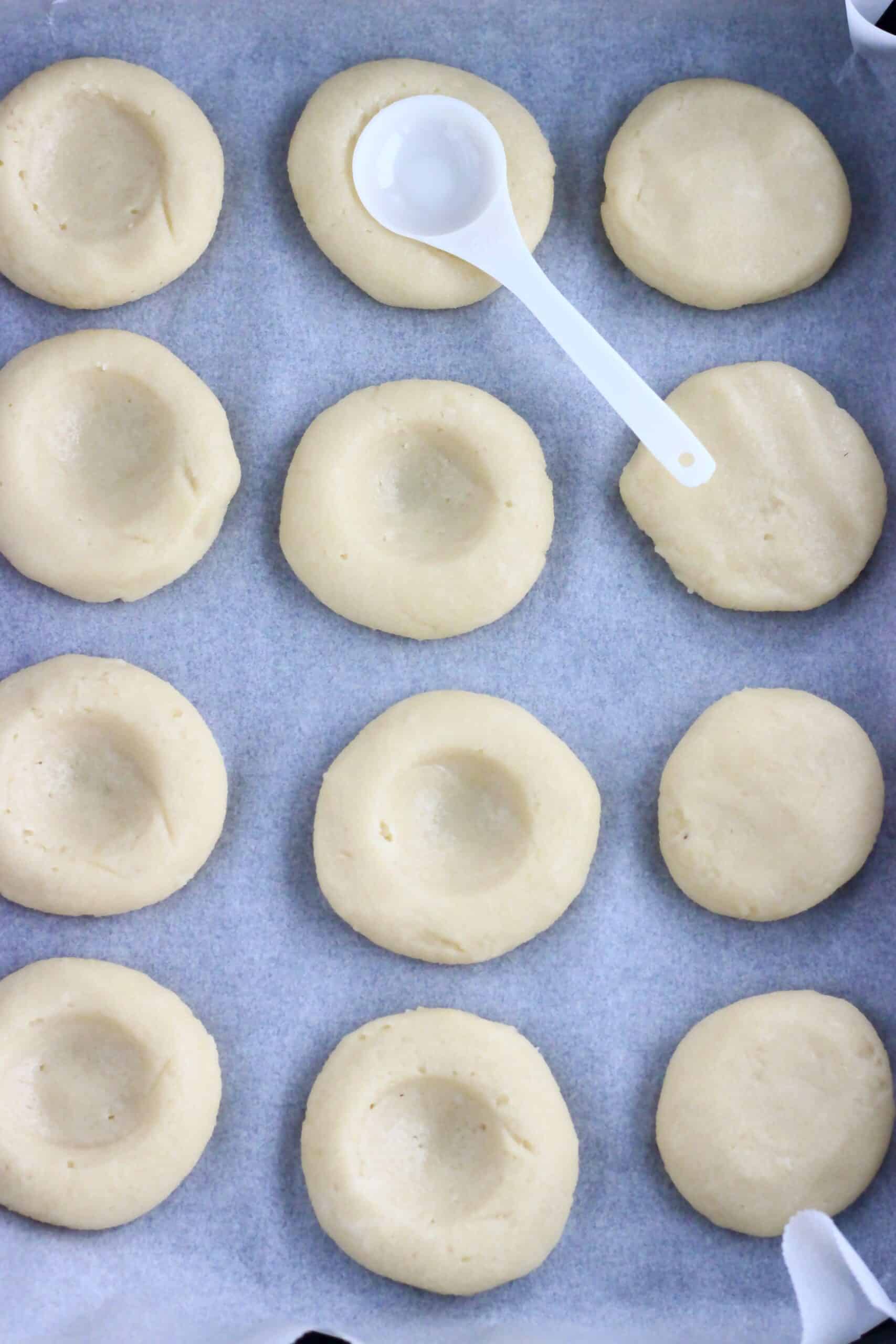 12 round vegan cookie dough patties on a baking tray lined with baking paper with a teaspoon making indents in the patties