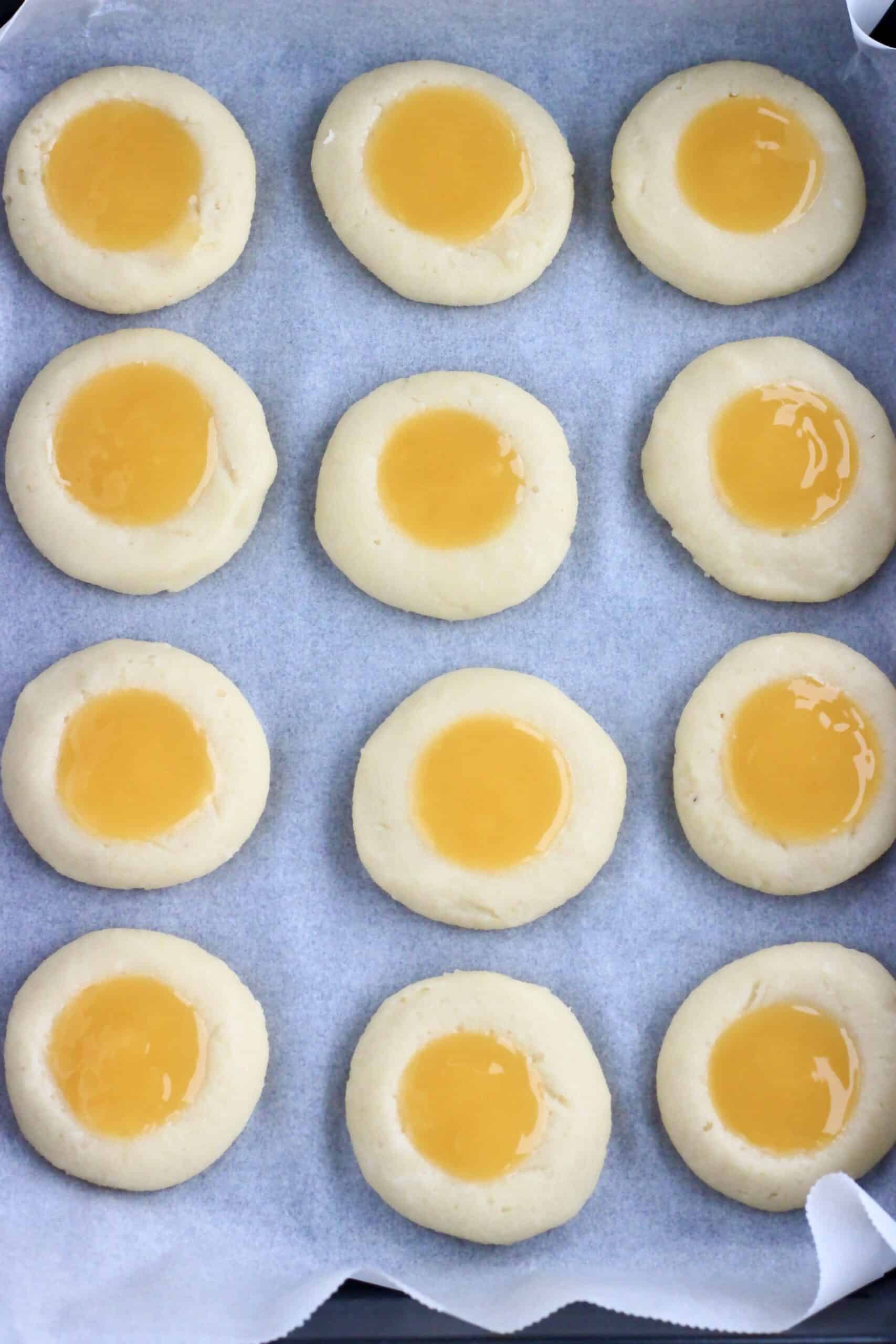 12 raw vegan lemon thumbprint cookies on a baking tray lined with baking paper