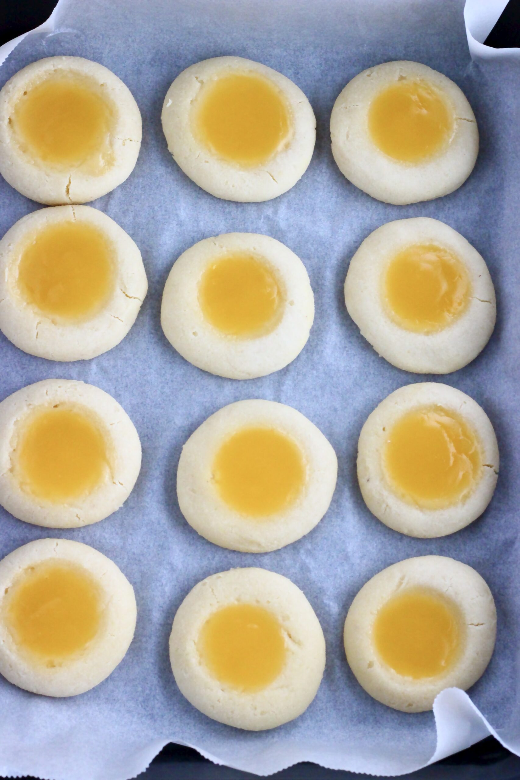 12 baked vegan lemon thumbprint cookies on a baking tray lined with baking paper