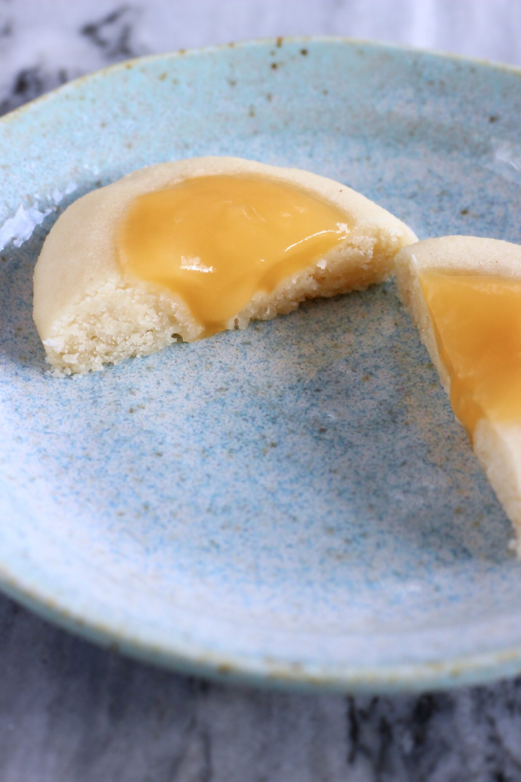 A vegan lemon thumbprint cookie cut in half on a plate