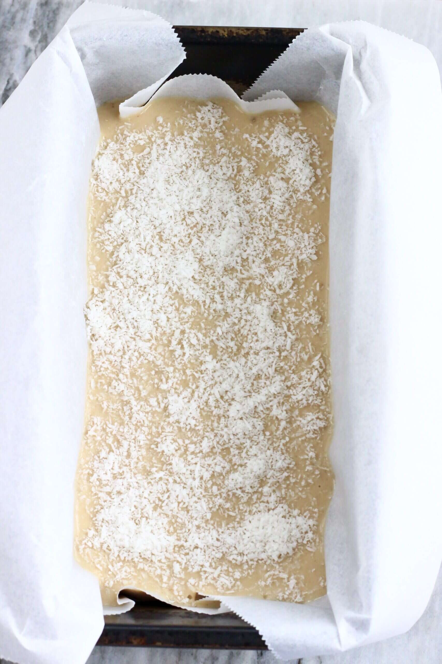 Raw vegan butter mochi batter sprinkled with desiccated coconut in a loaf tin lined with baking paper