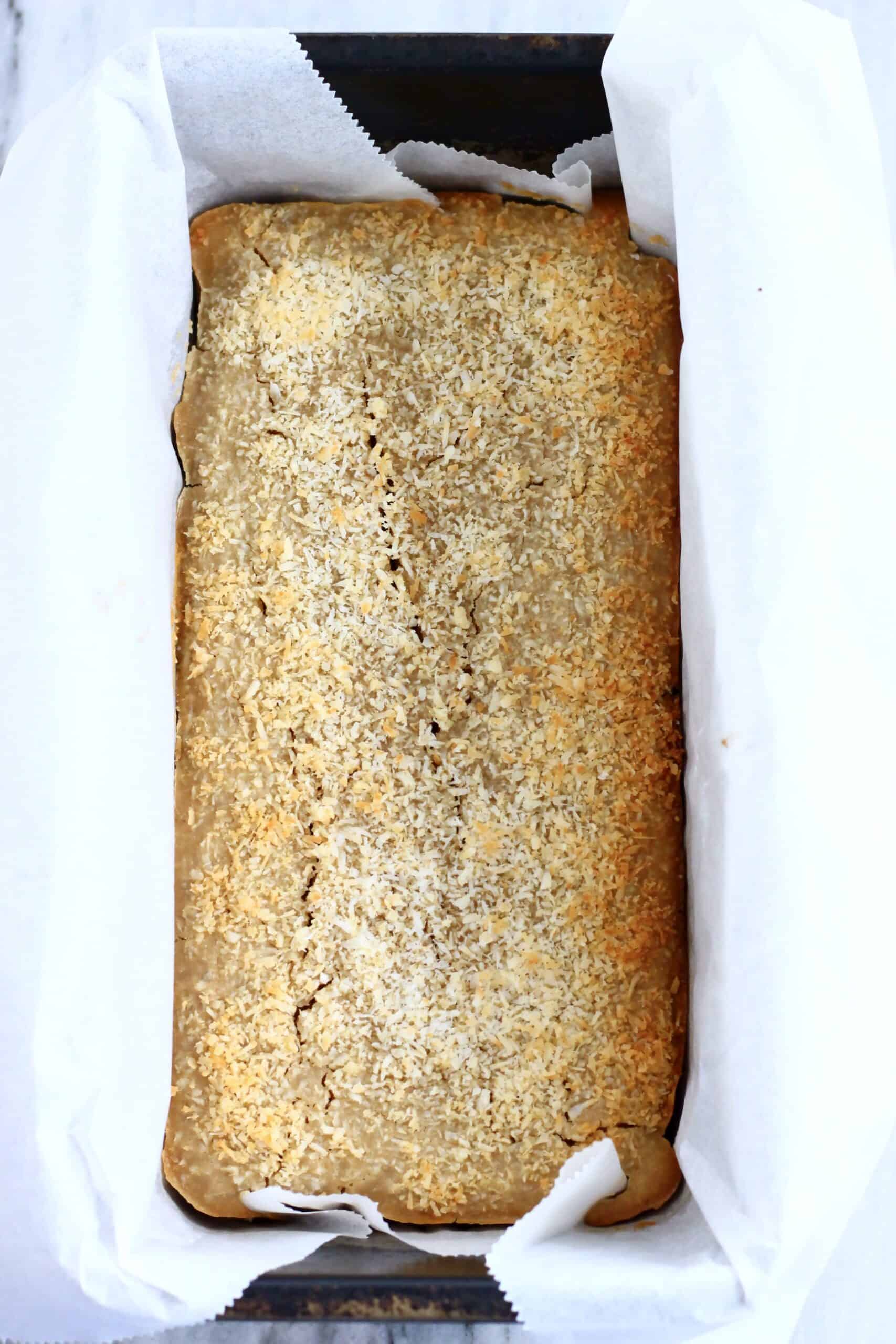 Baked vegan butter mochi topped with desiccated coconut in a loaf tin lined with baking paper