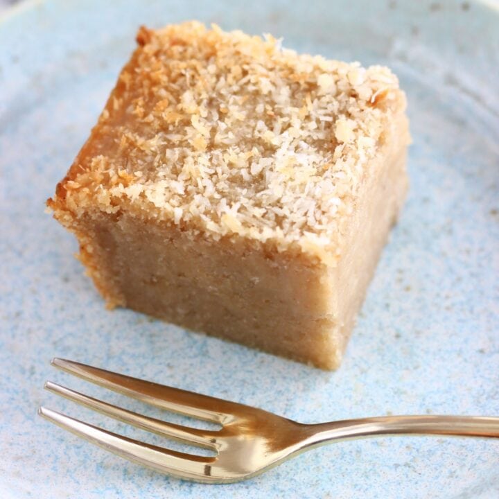 A square of vegan butter mochi topped with desiccated coconut on a plate with a fork