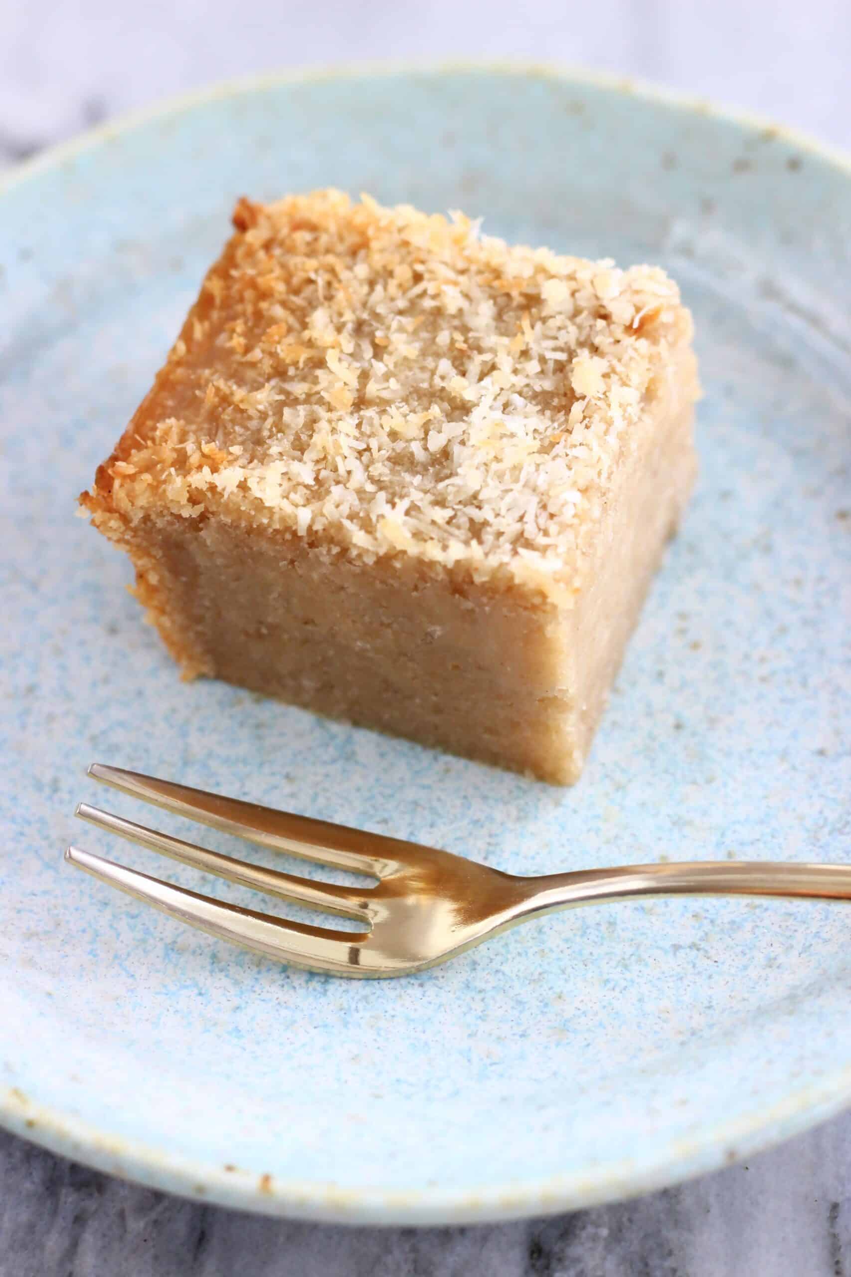 A square of vegan butter mochi topped with desiccated coconut on a plate with a fork
