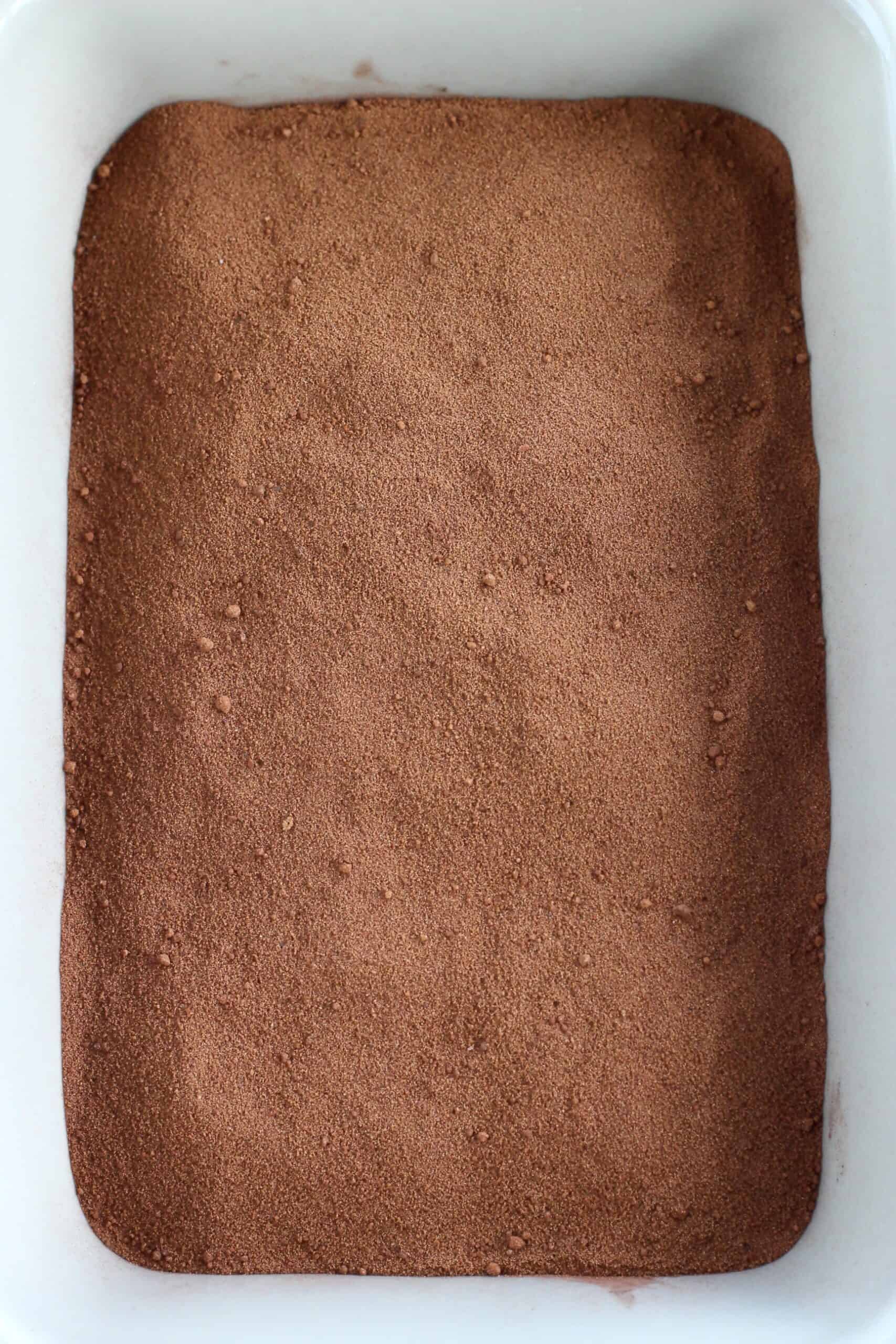 Vegan chocolate self-saucing pudding batter with cocoa powder and sugar sprinkled on top in a rectangular baking dish