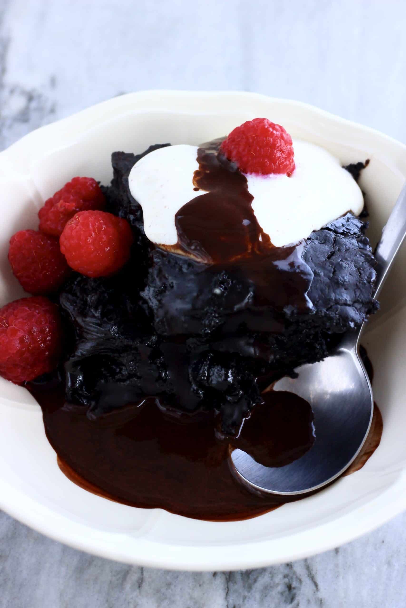 Vegan chocolate self-saucing pudding in a bowl with cream and raspberries