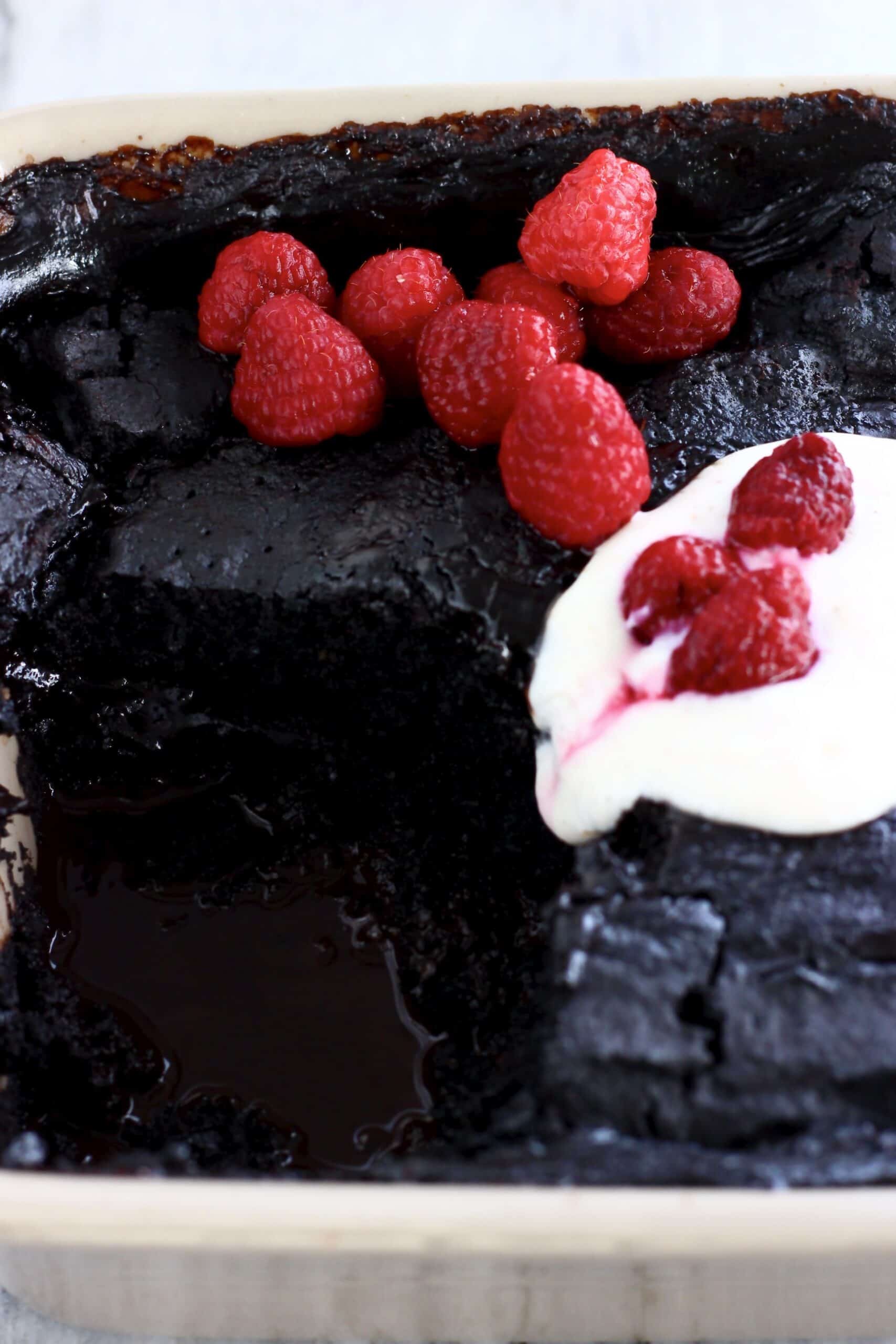 Vegan chocolate self-saucing pudding in a baking dish topped with cream and raspberries