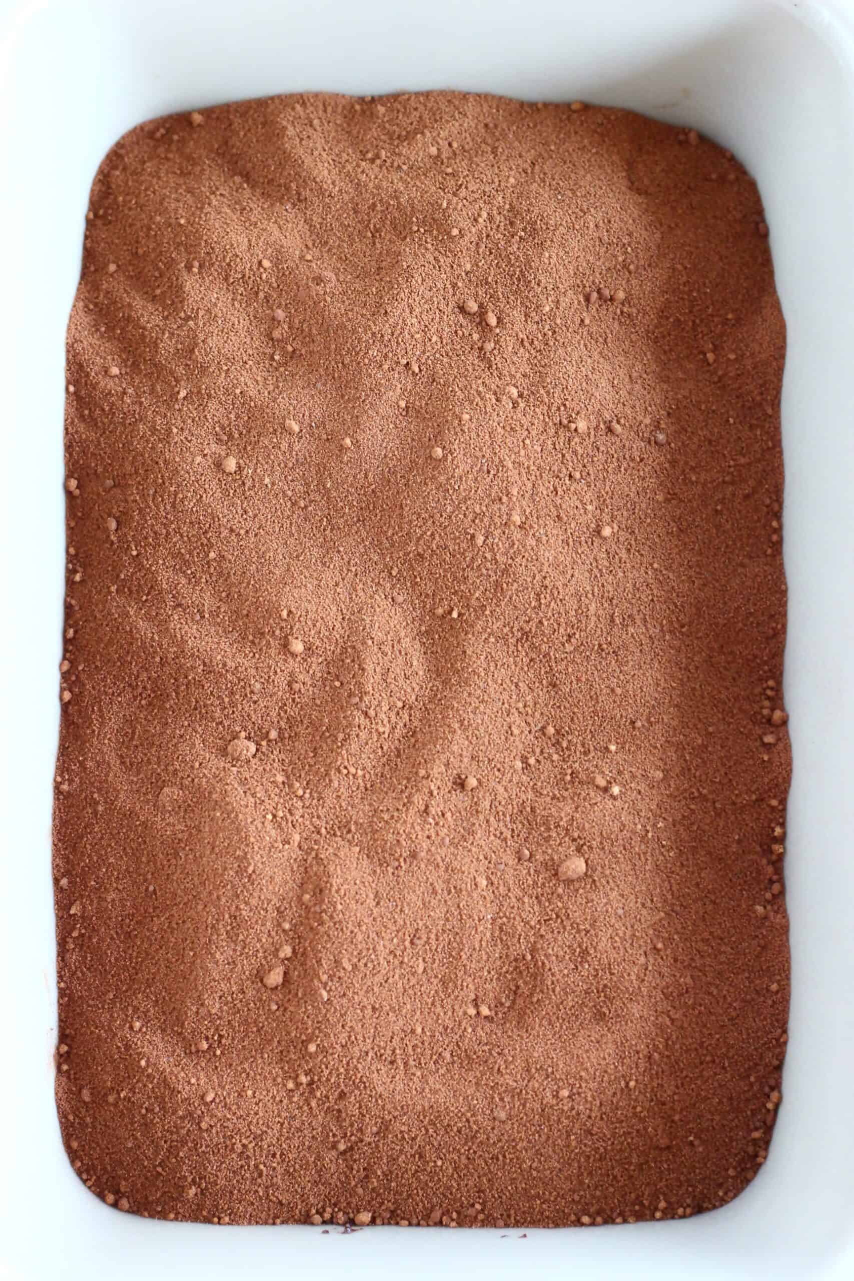 Cocoa powder and coconut sugar sprinkled over raw vegan chocolate fudge pudding batter in a rectangular baking dish