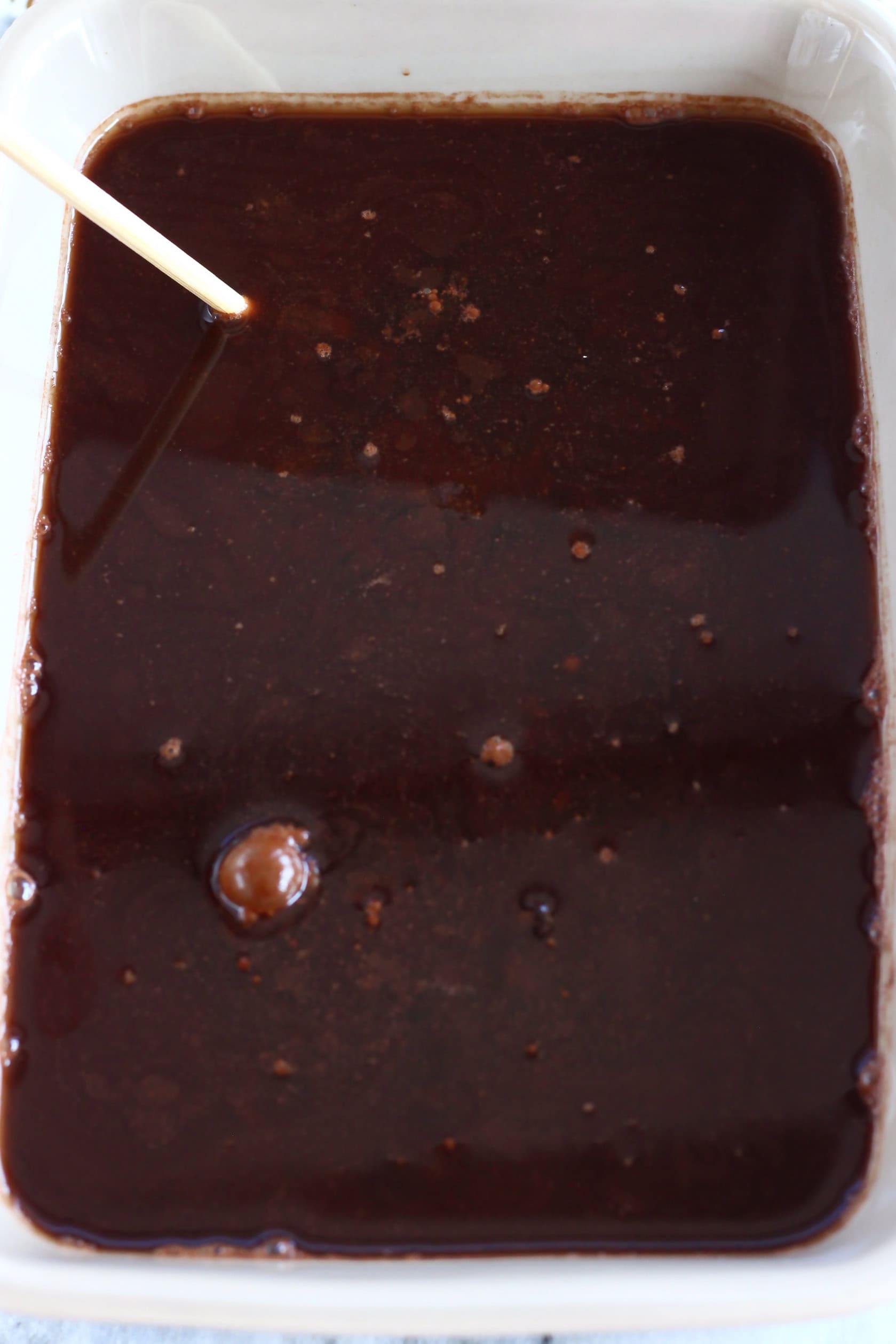 Raw vegan chocolate fudge pudding with hot water in a rectangular baking dish with a skewer inside it