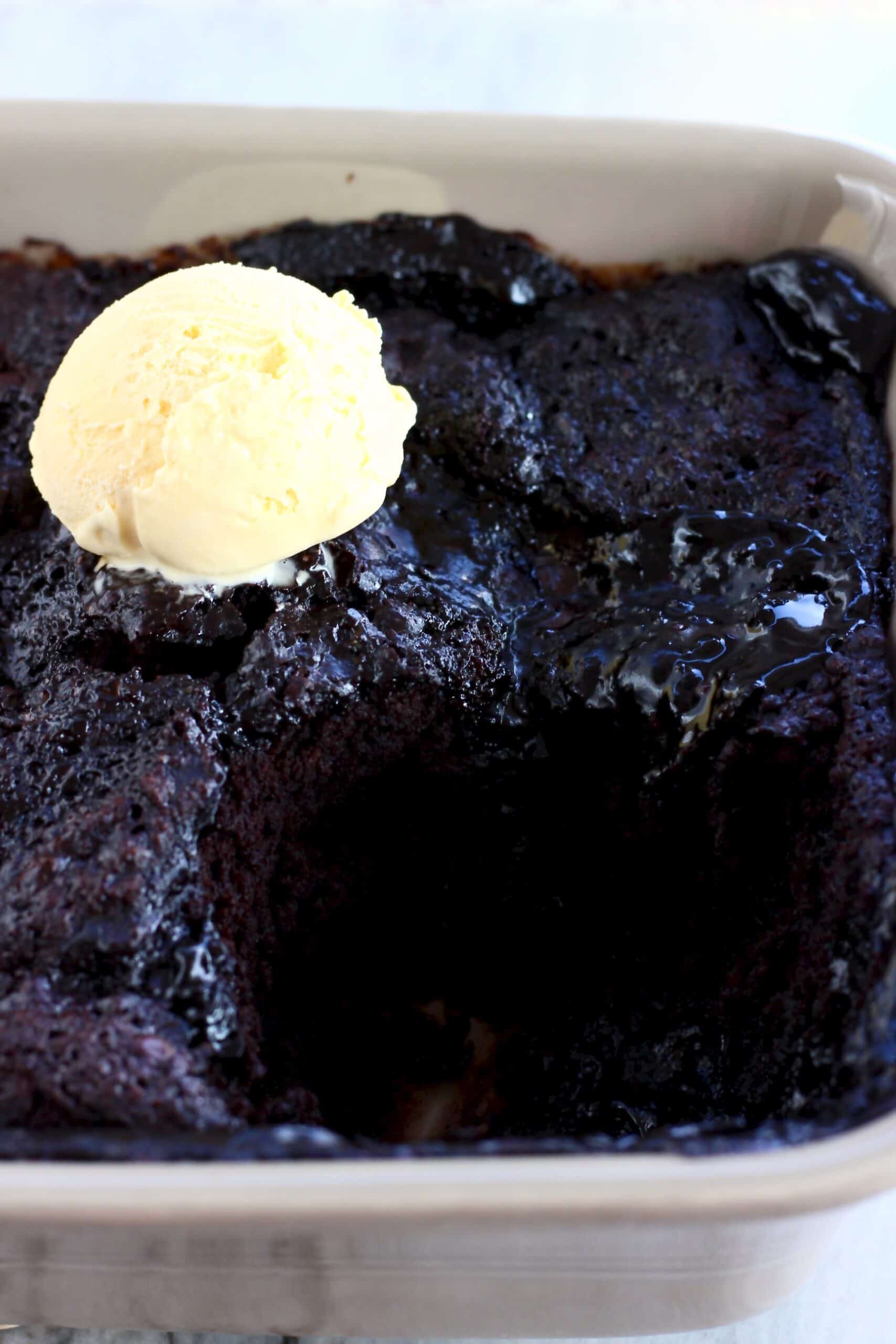 Vegan chocolate fudge pudding in a baking dish with a scoop of vanilla ice cream