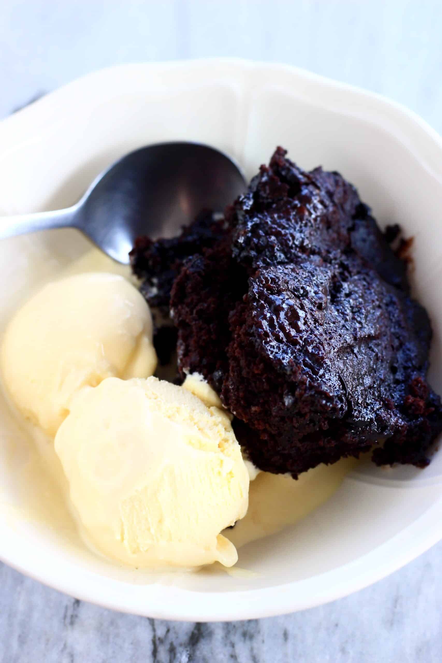 Vegan chocolate fudge pudding in a bowl with two scoops of vanilla ice cream and a spoon
