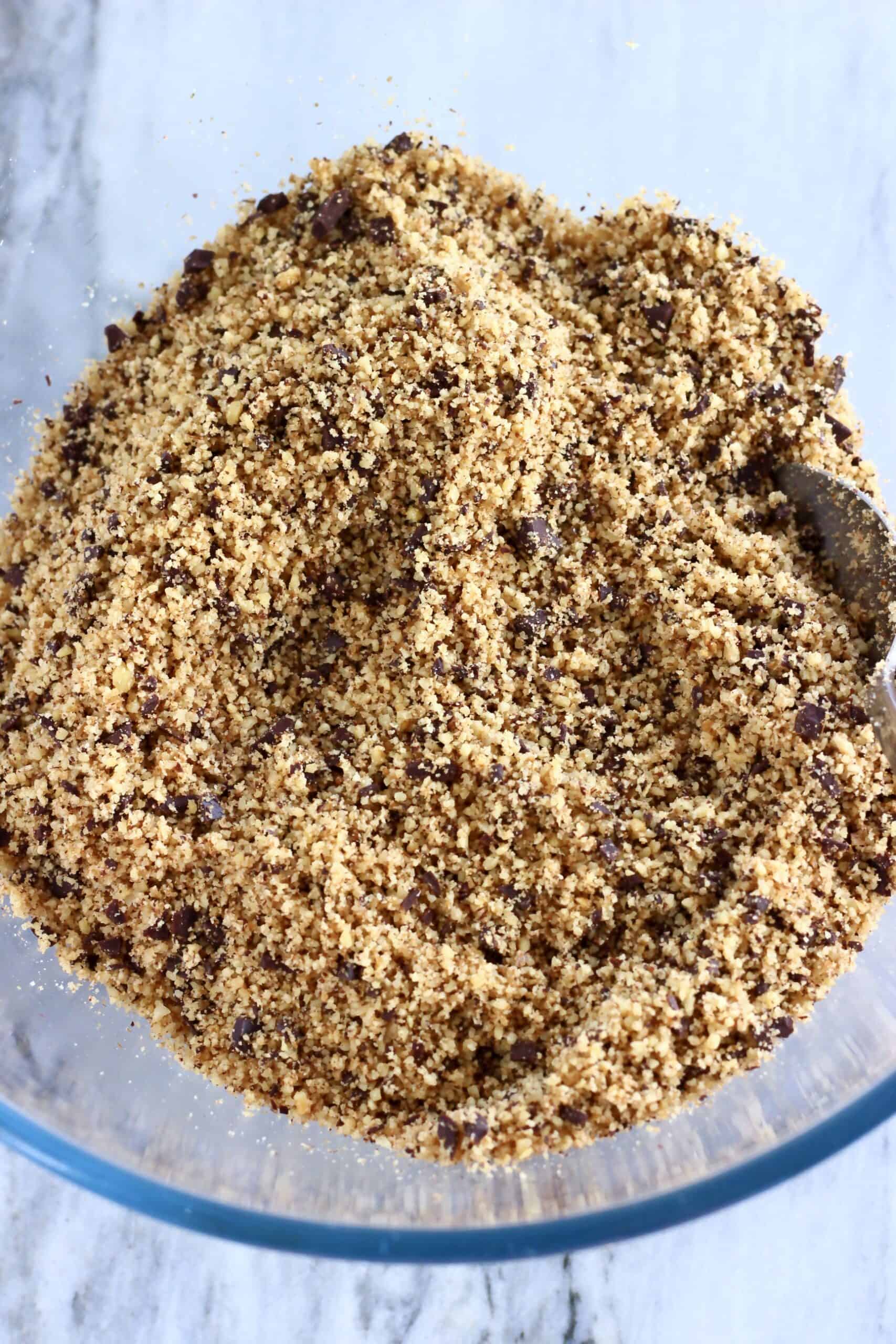 Ground walnuts, coconut sugar and chopped dark chocolate in a bowl with a spoon