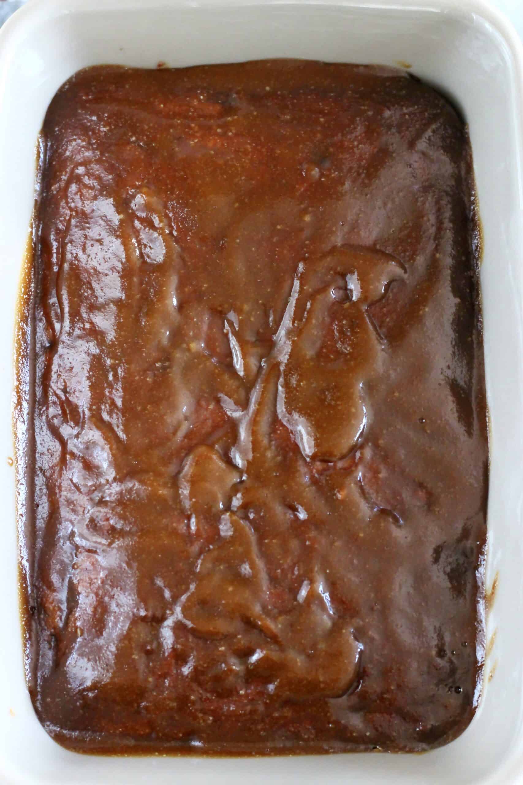 Vegan sticky toffee pudding topped with toffee sauce in a rectangular baking dish