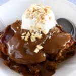 Vegan sticky toffee pudding in a bowl with a scoop of vanilla ice cream and a spoon