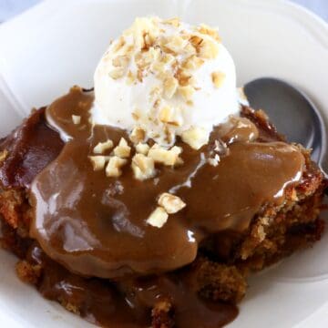 Vegan sticky toffee pudding in a bowl with a scoop of vanilla ice cream and a spoon