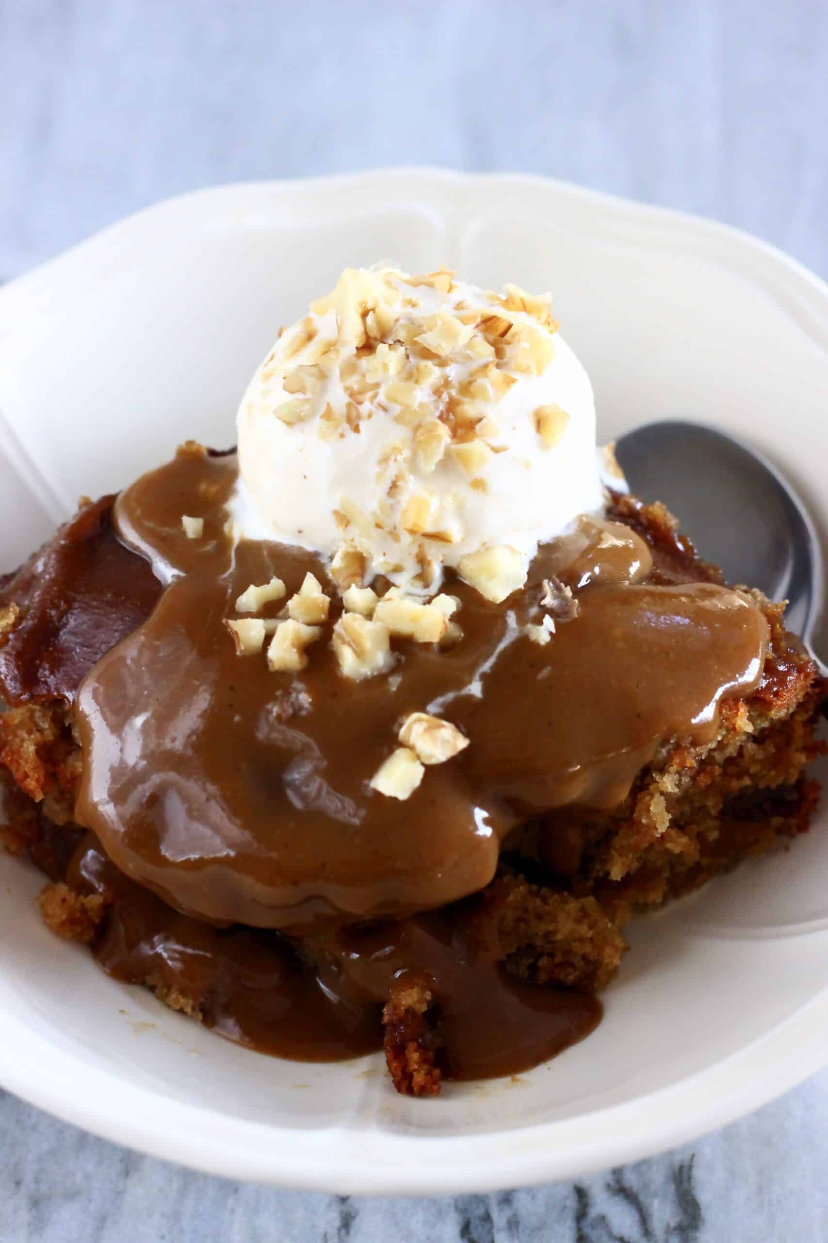 Vegan sticky toffee pudding in a bowl with a scoop of vanilla ice cream and a spoon