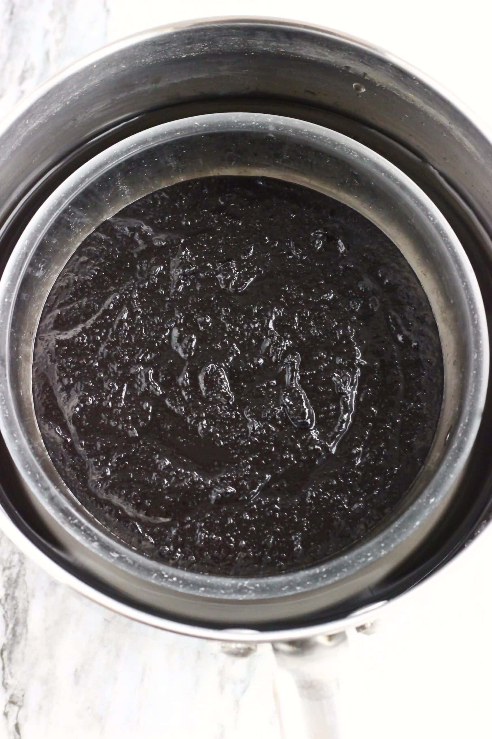 Raw vegan chocolate Christmas pudding batter in a glass bowl in a saucepan with water in it