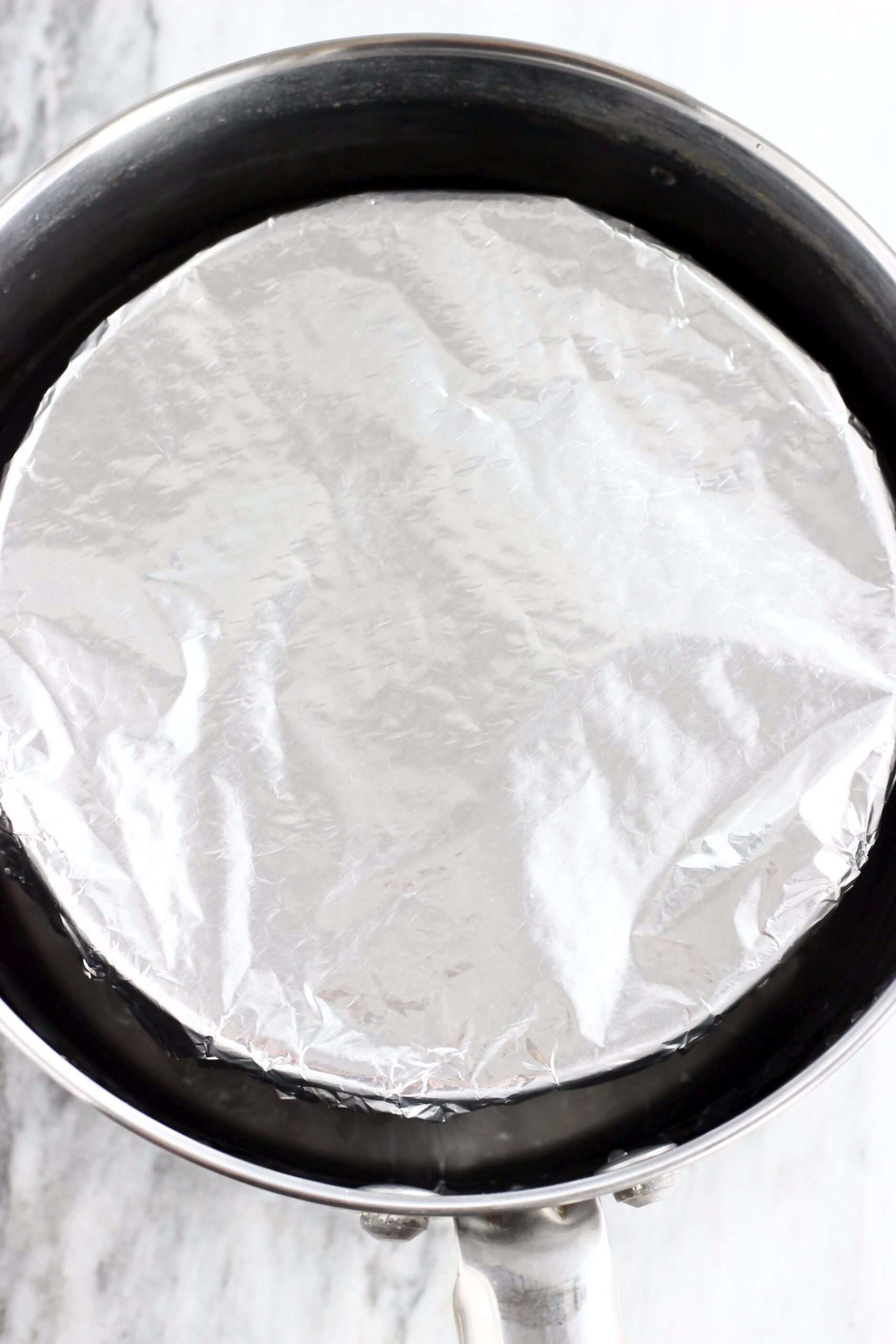 A bowl filled with vegan chocolate Christmas pudding batter covered with tin foil in a saucepan with water in it