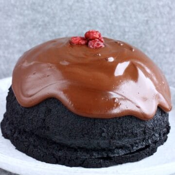 A vegan chocolate Christmas pudding covered with chocolate sauce on a plate