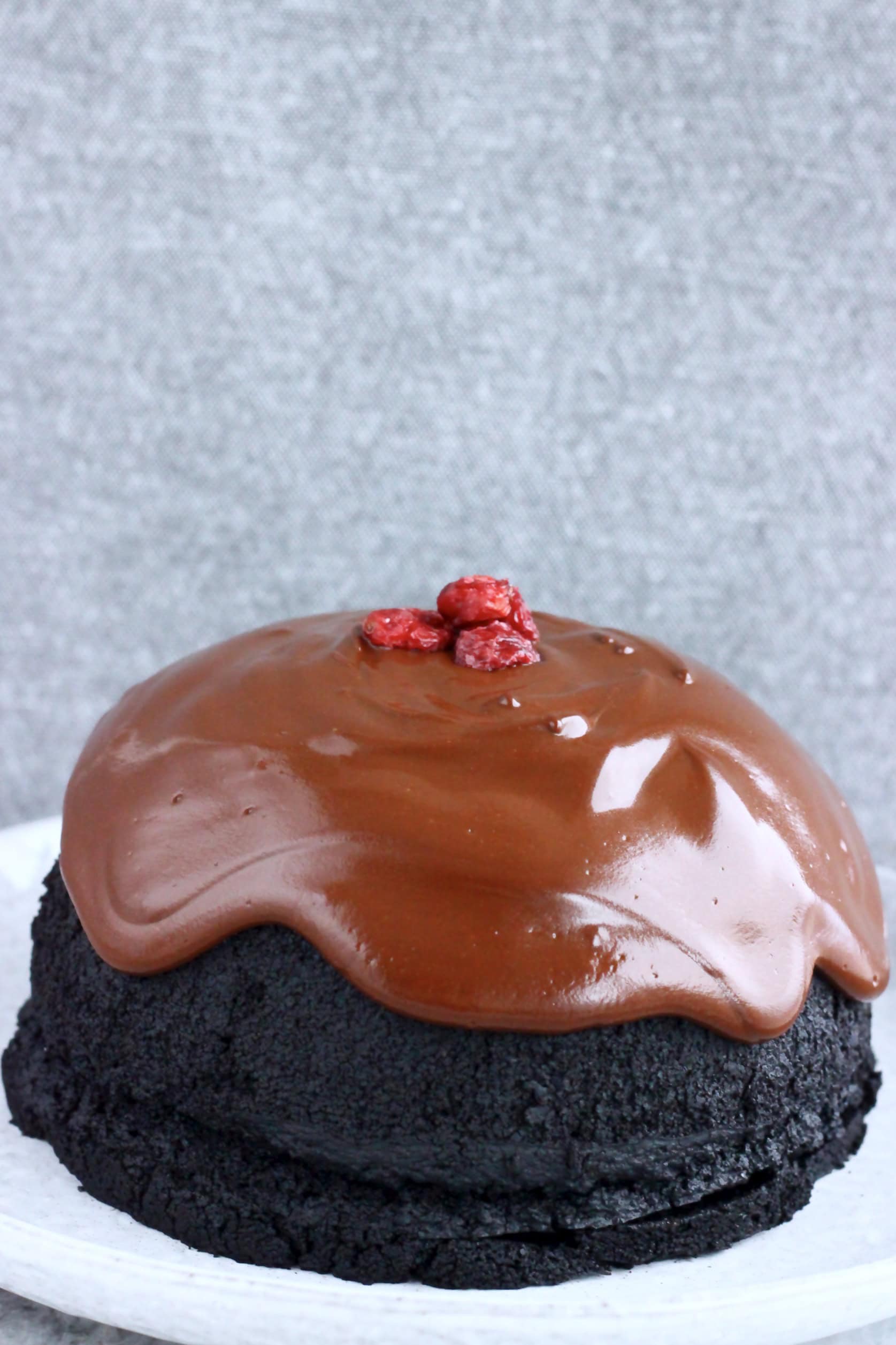 A vegan chocolate Christmas pudding covered with chocolate sauce on a plate