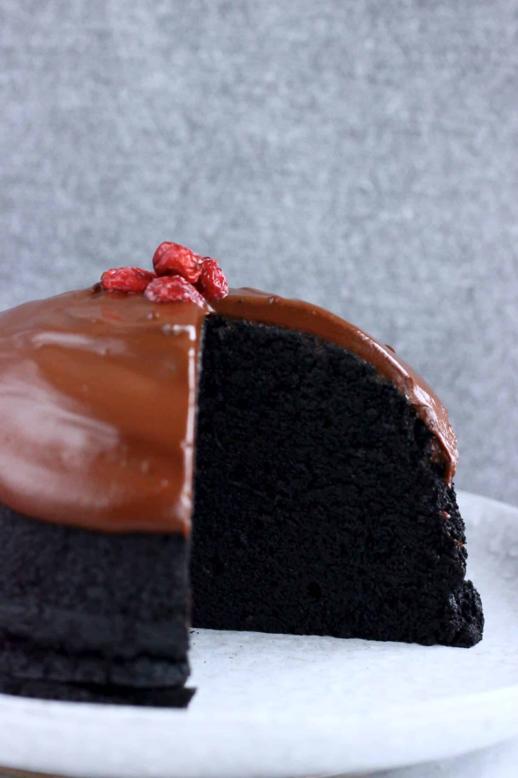 A vegan chocolate Christmas pudding covered in chocolate sauce with a slice cut out of it